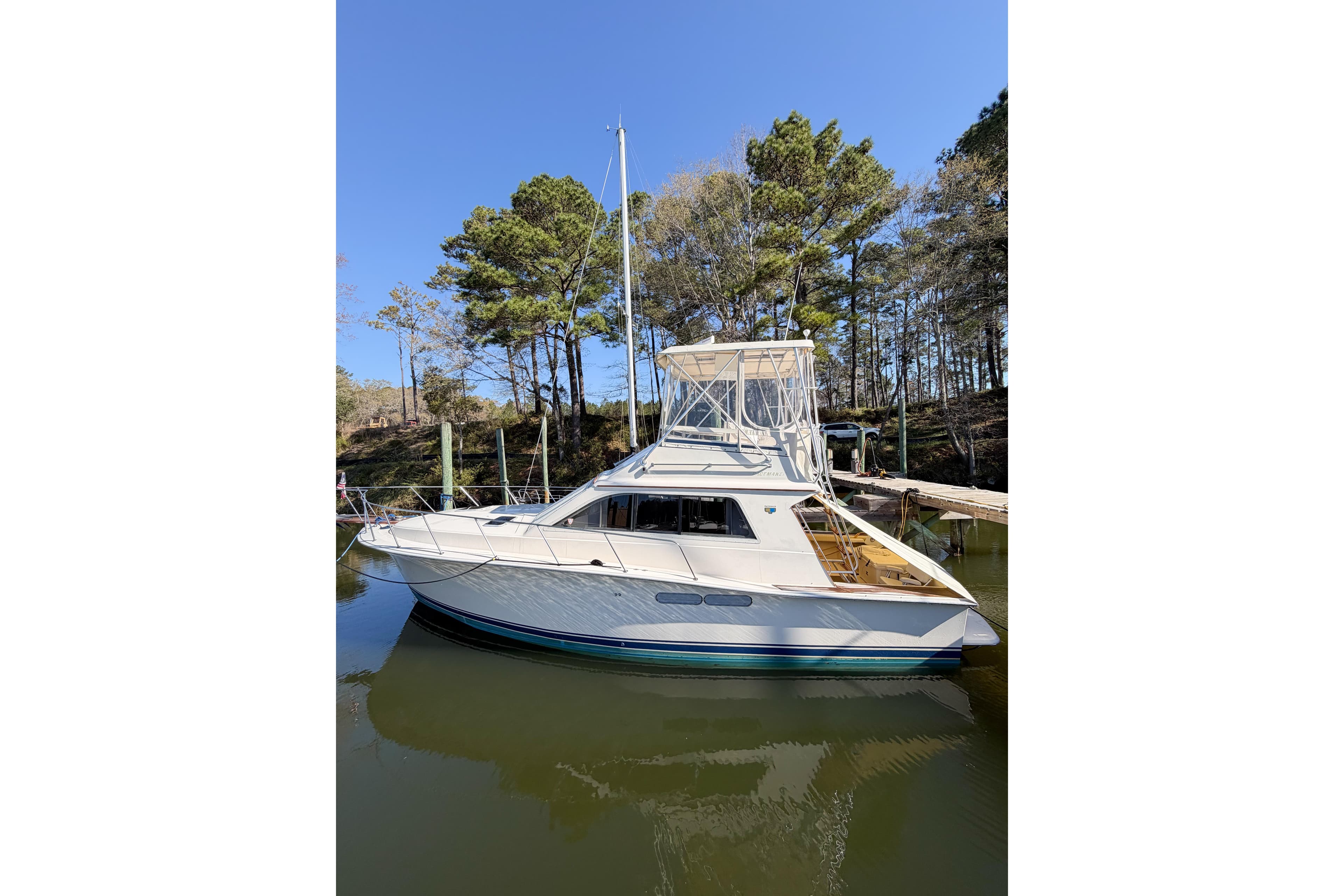 1988 Pacemaker 36 Convertible yacht docked by a wooded shoreline.