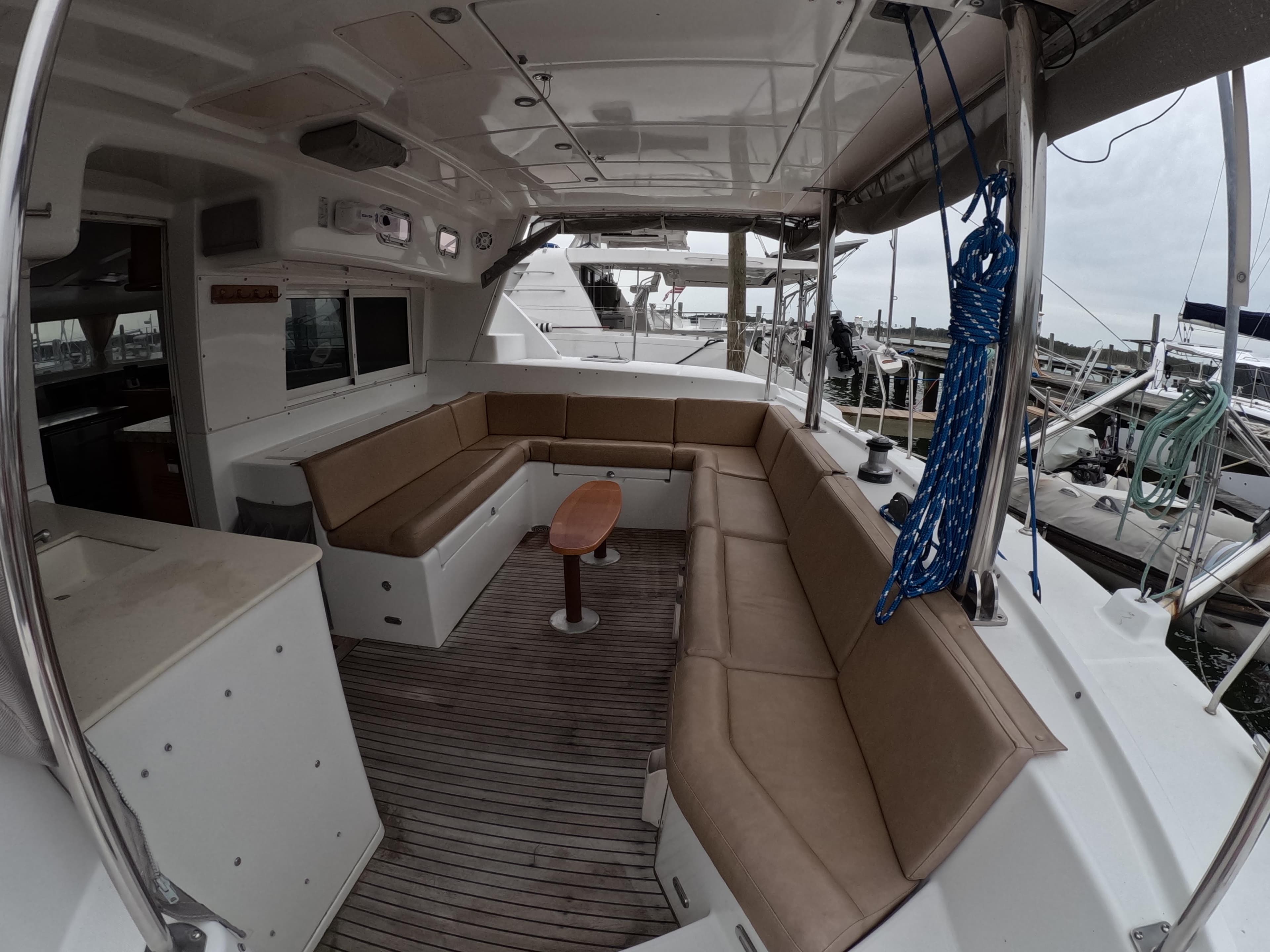 Spacious seating area on a 2006 Lagoon 440 catamaran, featuring comfortable cushions and a wooden table.