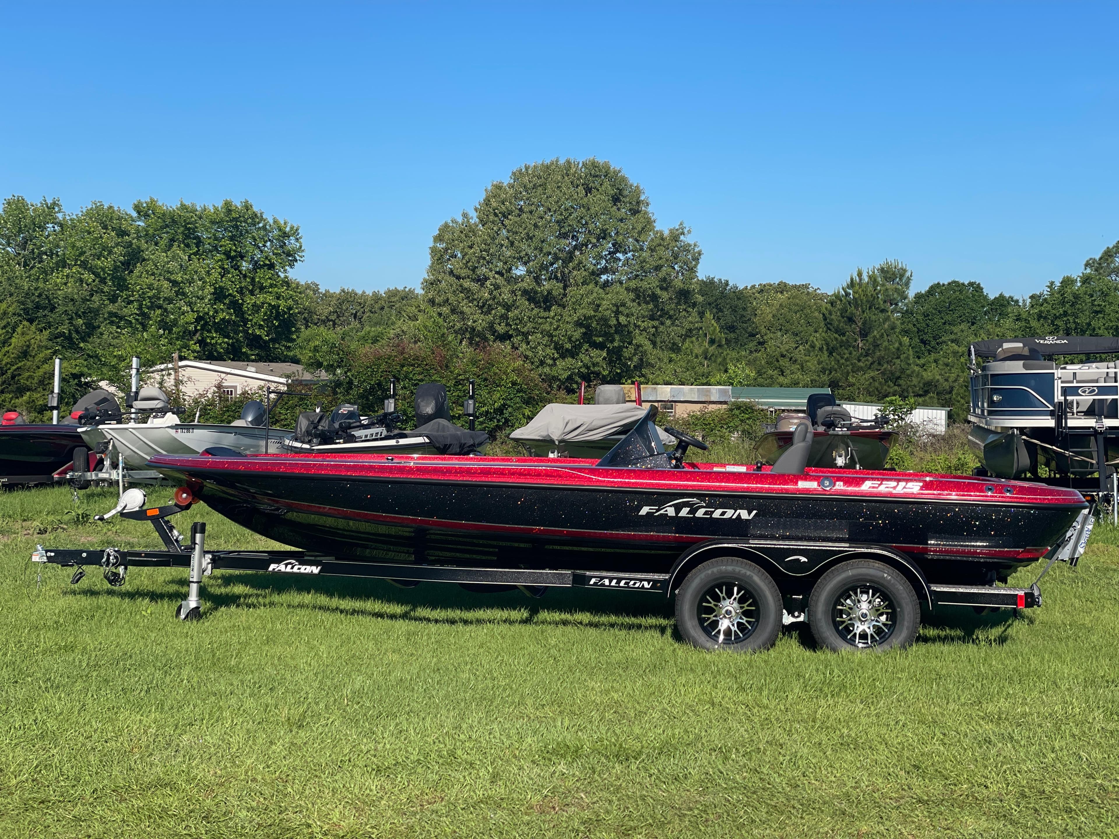 2025 Falcon Boats F215 on trailer, parked on grass with trees in background.