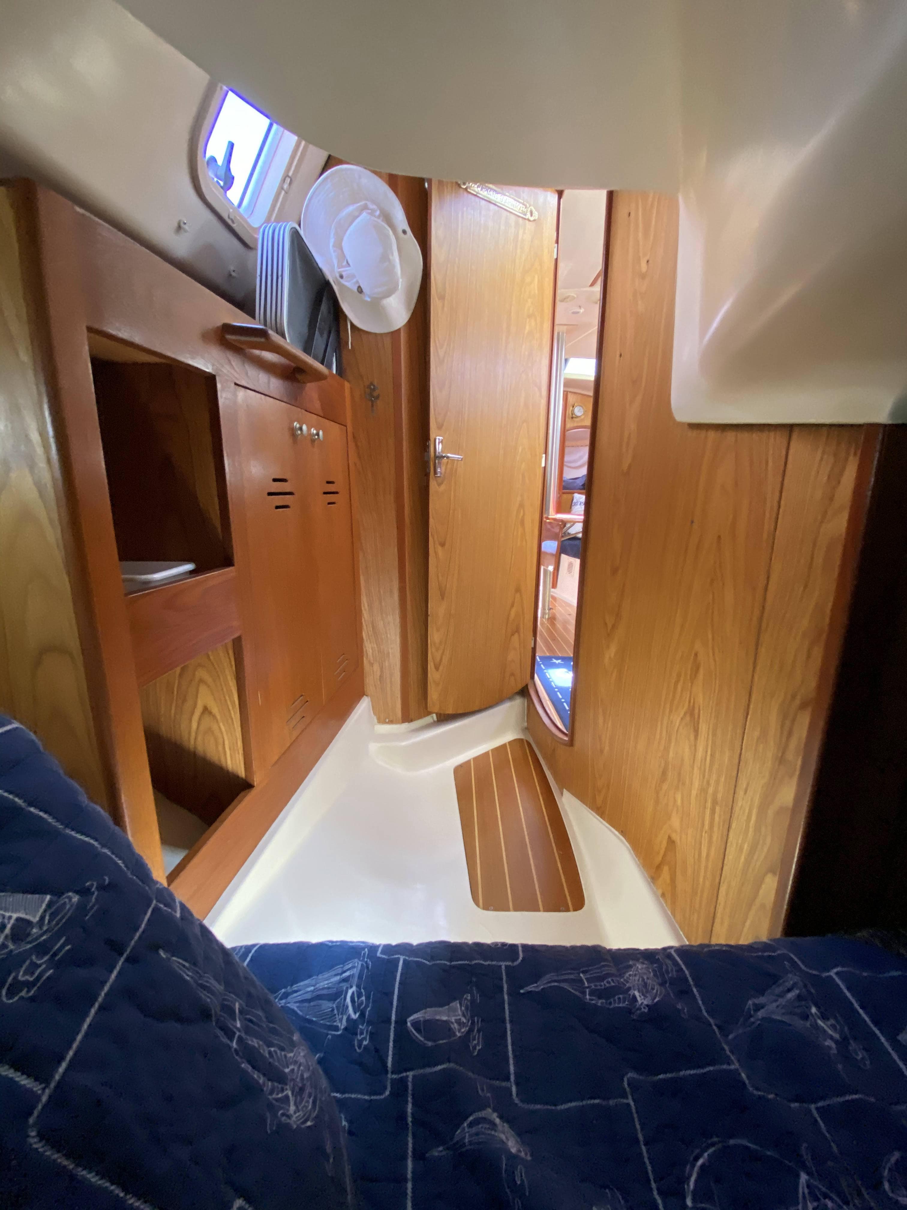 Interior of 2001 Hunter 320 sailboat with wooden cabinetry and blue patterned bedding.
