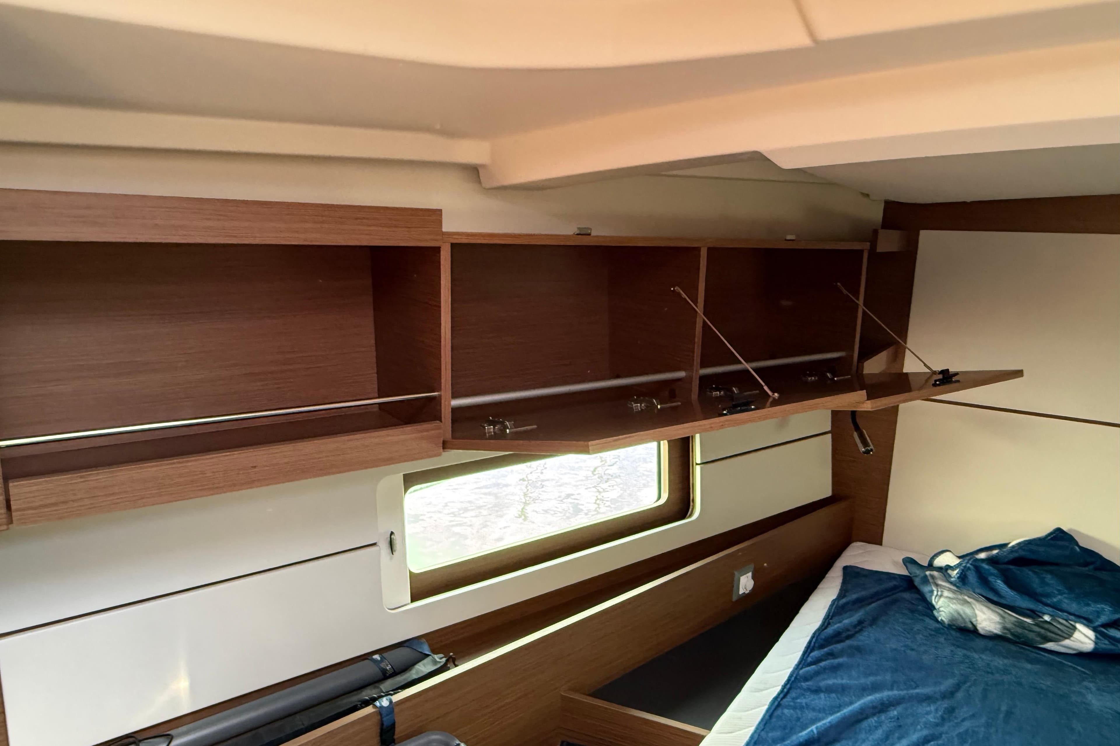 Interior of 2020 Beneteau Oceanis 46.1 yacht with open wooden cabinets and a cozy bed.
