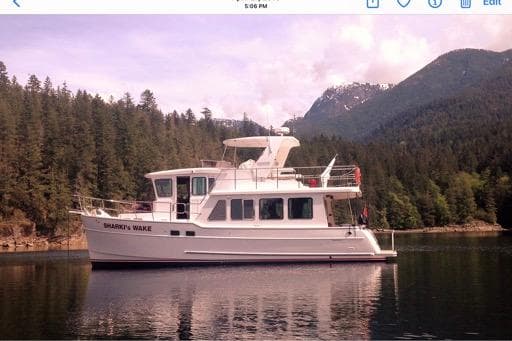 2016 North Pacific 45 Pilothouse yacht on serene lake with forested mountains.