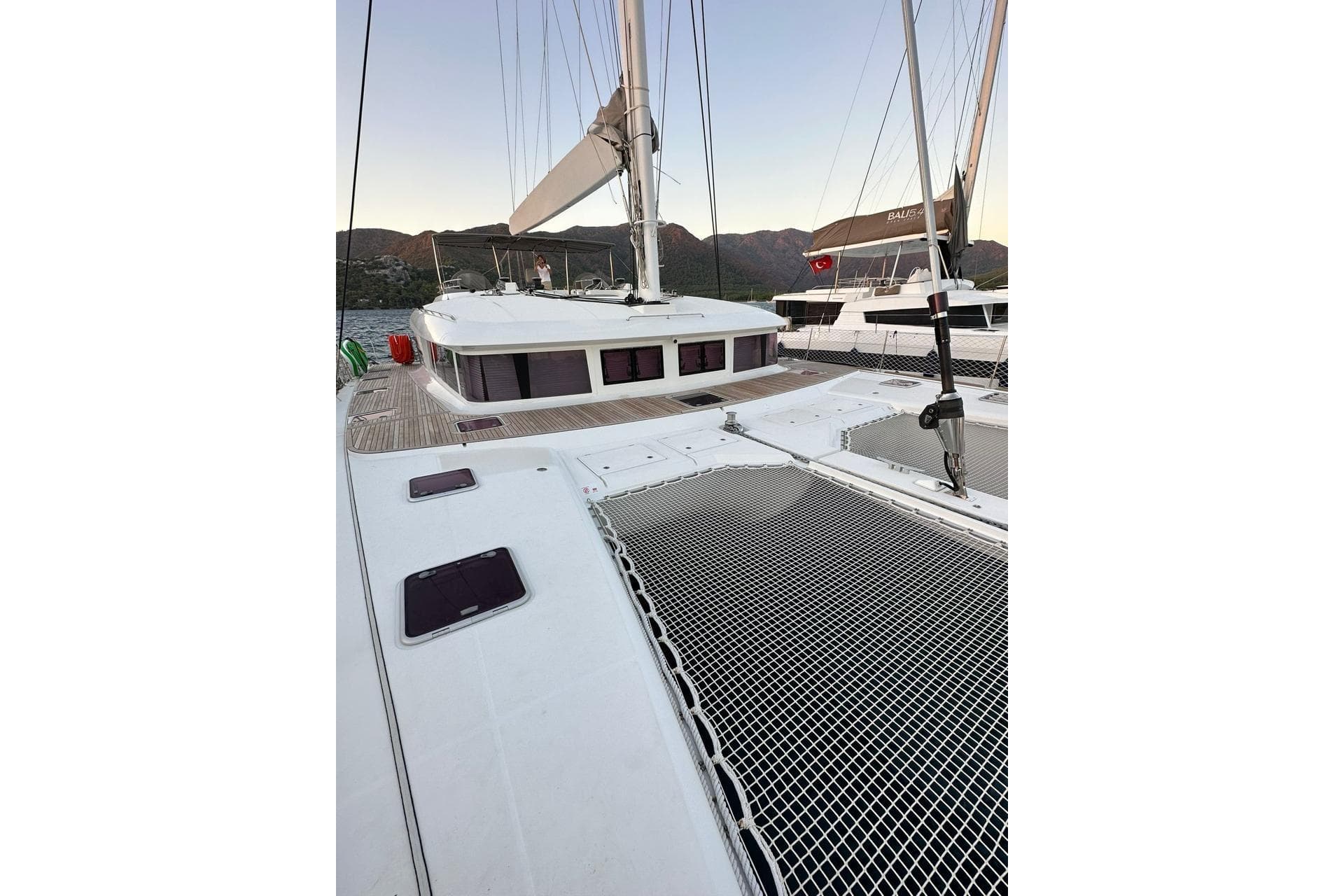 2013 Lagoon 620 catamaran deck with netting, docked near scenic mountains.
