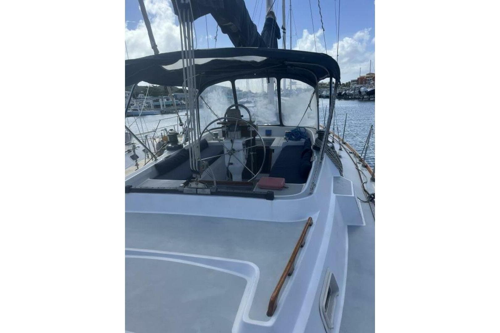 1982 C&C Landfall sailboat cockpit with steering wheel, docked at marina under blue sky.