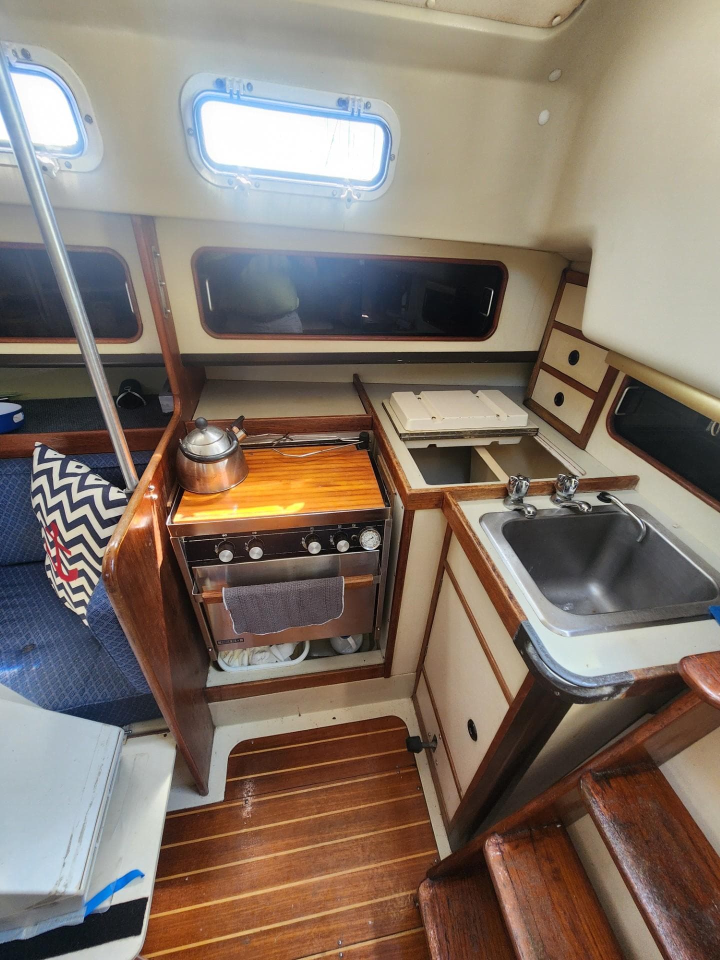 Interior of 1982 C&C 34 sailboat galley with stove, sink, and wooden cabinetry.