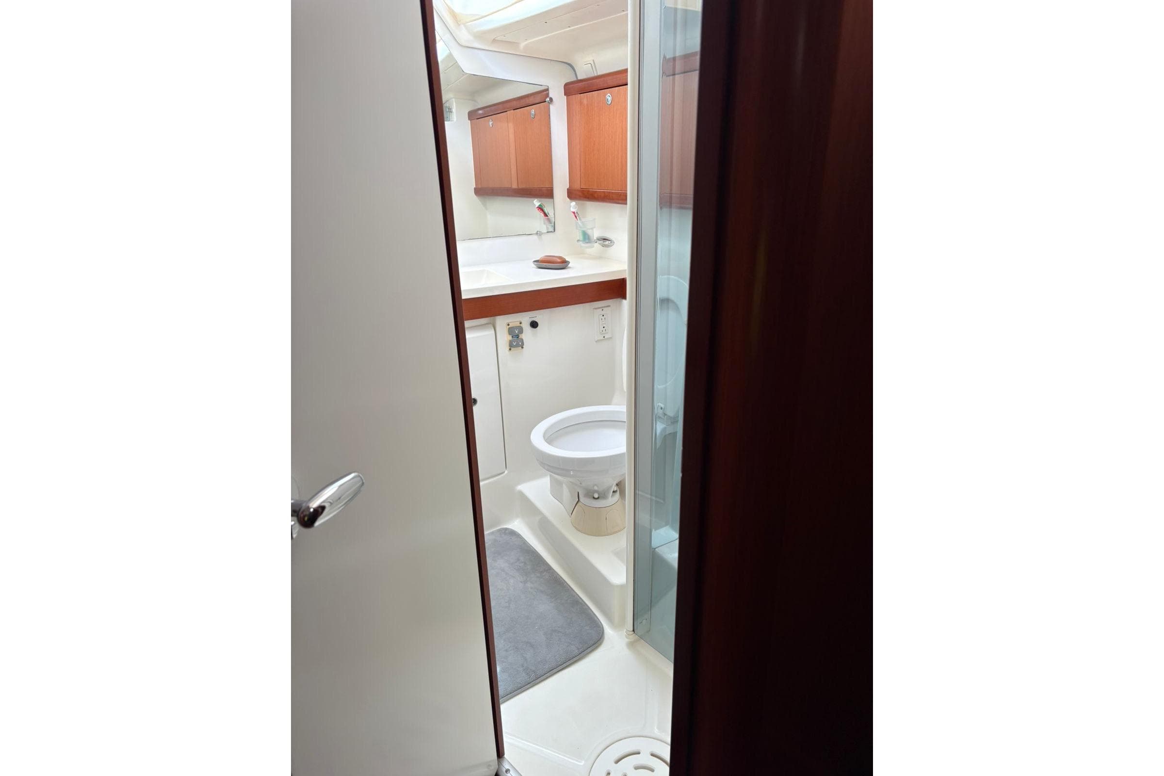 Bathroom interior of 2008 Beneteau 49 yacht, featuring toilet and wooden cabinetry.