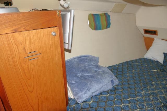 Cozy cabin interior of 2000 Hunter 460 sailboat with wooden cabinet and blue bedding.