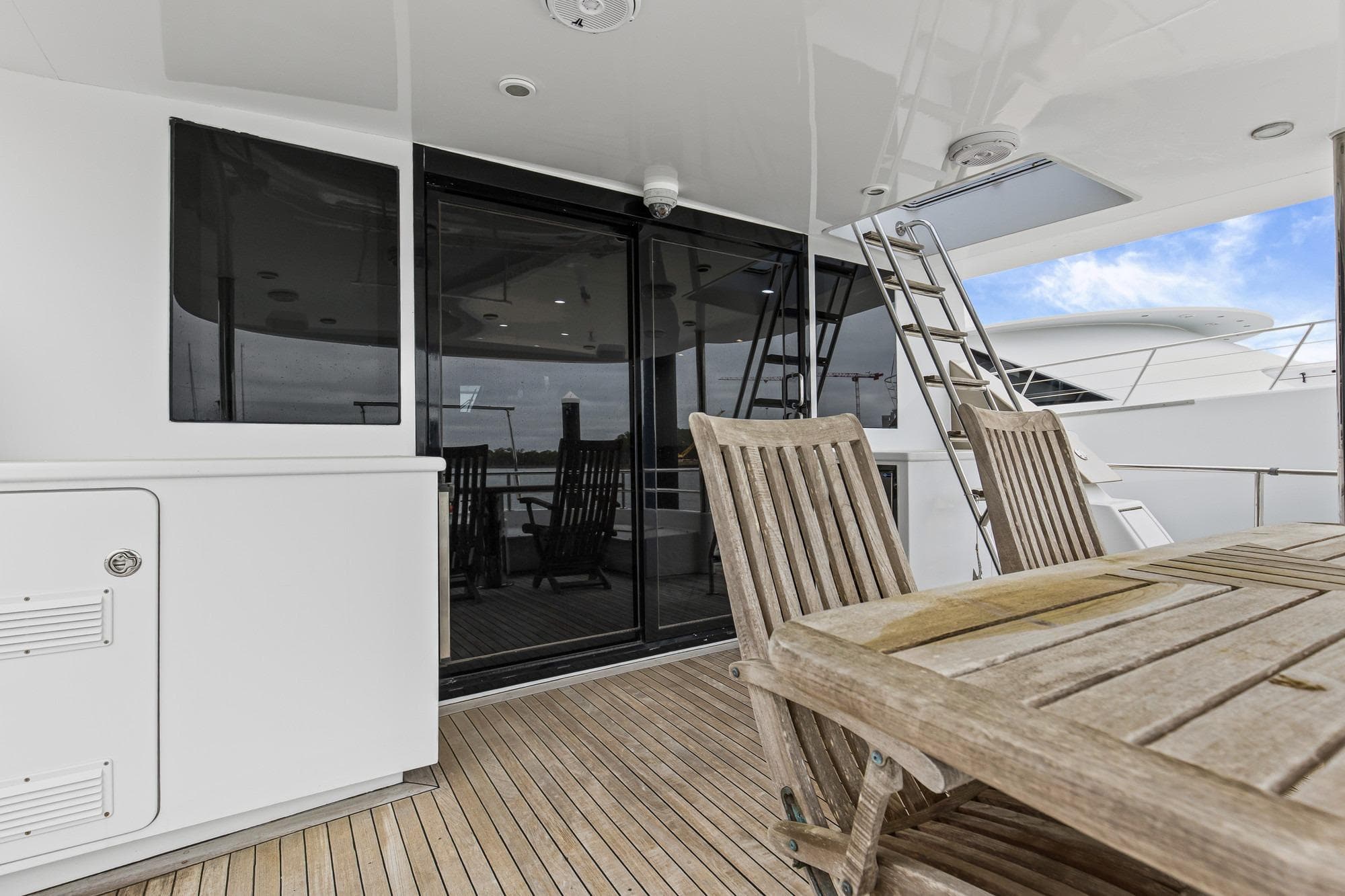 Luxury yacht deck with wooden furniture, glass doors, and ladder; Queenship 76 Baretta, 2004 model.