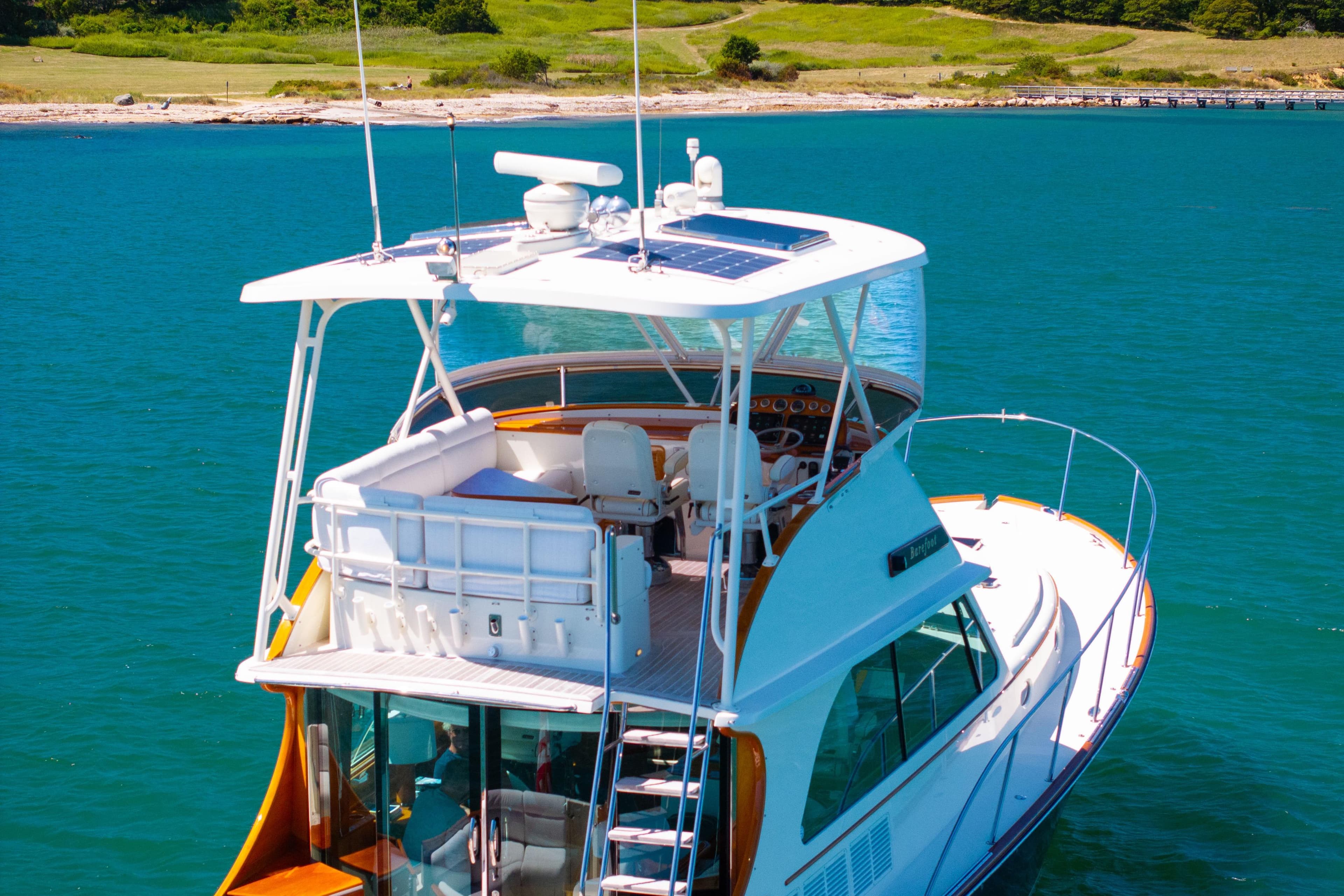 2014 Hinckley Talaria 48 Flybridge yacht on clear blue water, near a scenic shoreline.
