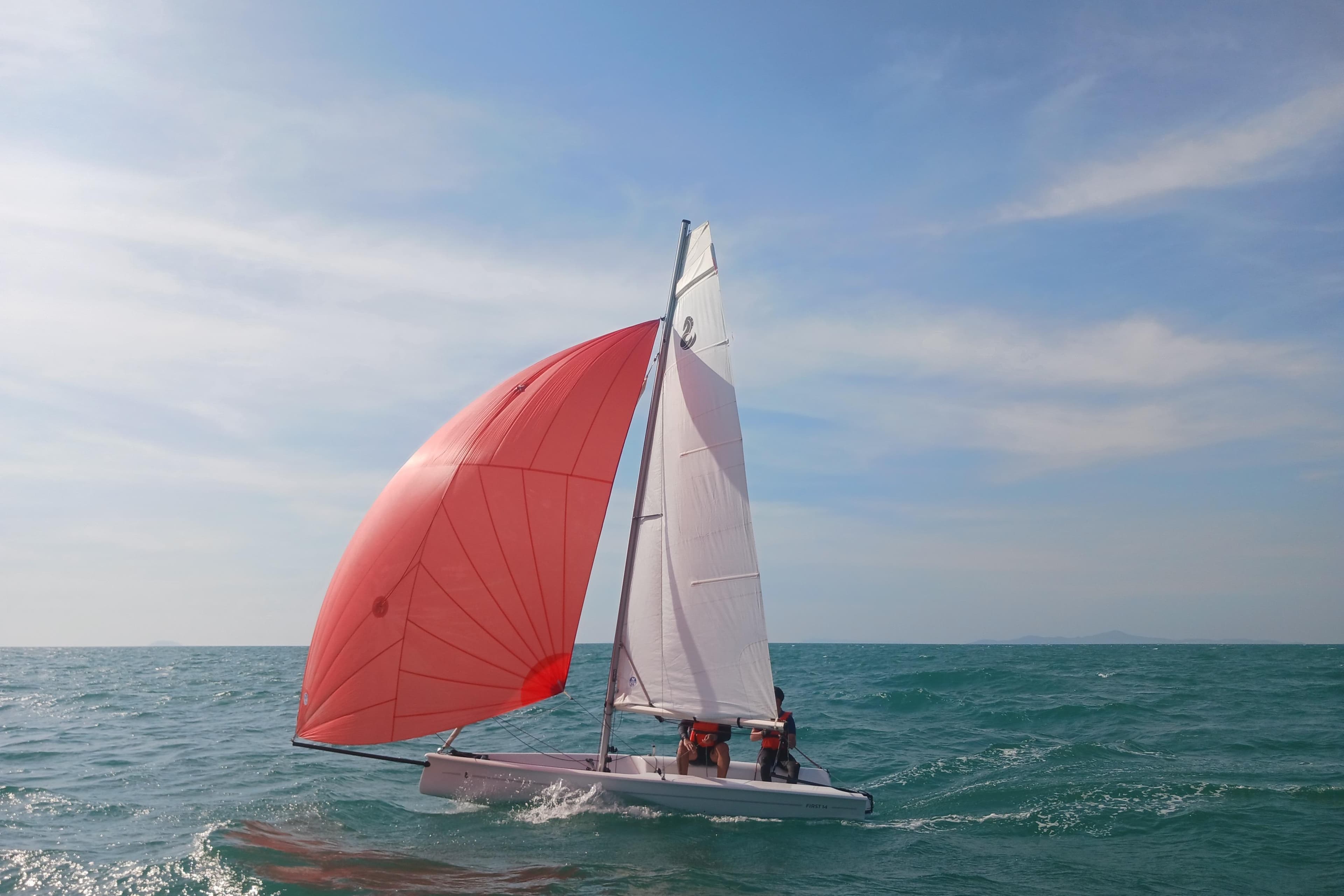 Sailing Beneteau First 14, 2021 model, with red spinnaker on open sea.