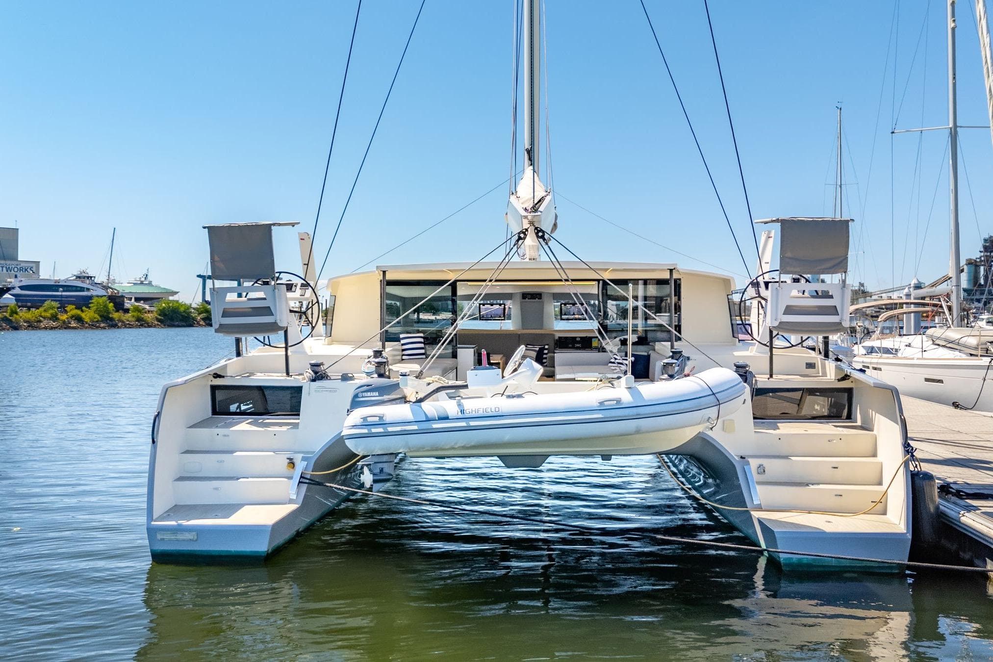 2019 Itacatamarans 14.99 catamaran docked with inflatable boat, sunny marina setting.