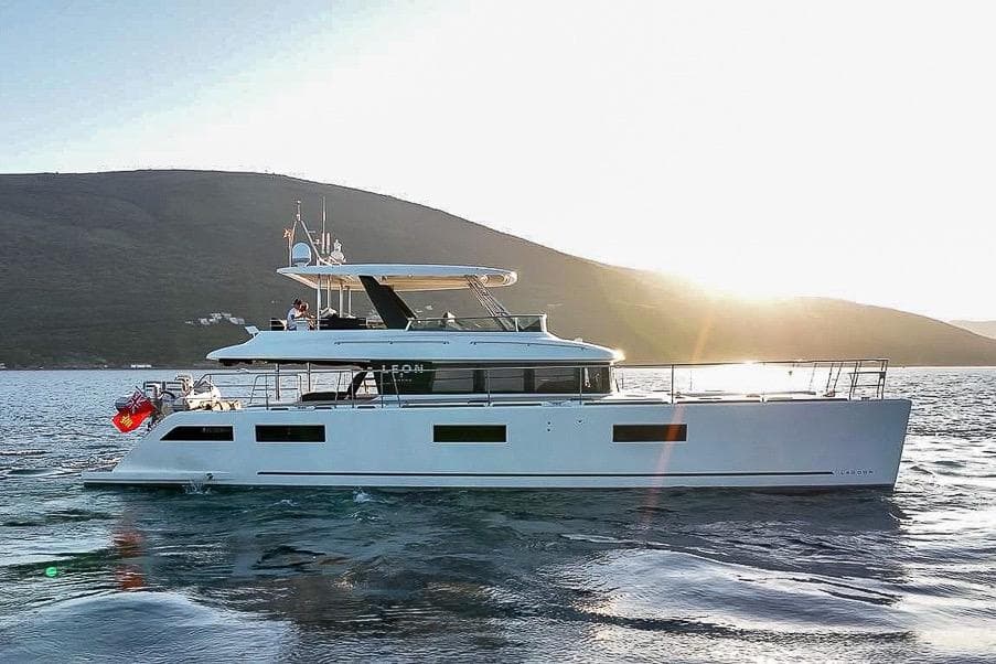 2020 Lagoon 630 MY yacht cruising at sunset near a mountainous coastline.