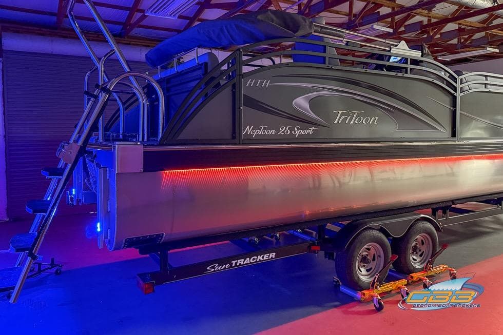 2026 JC 25 Neptoon LG pontoon boat with vibrant LED lighting on trailer.