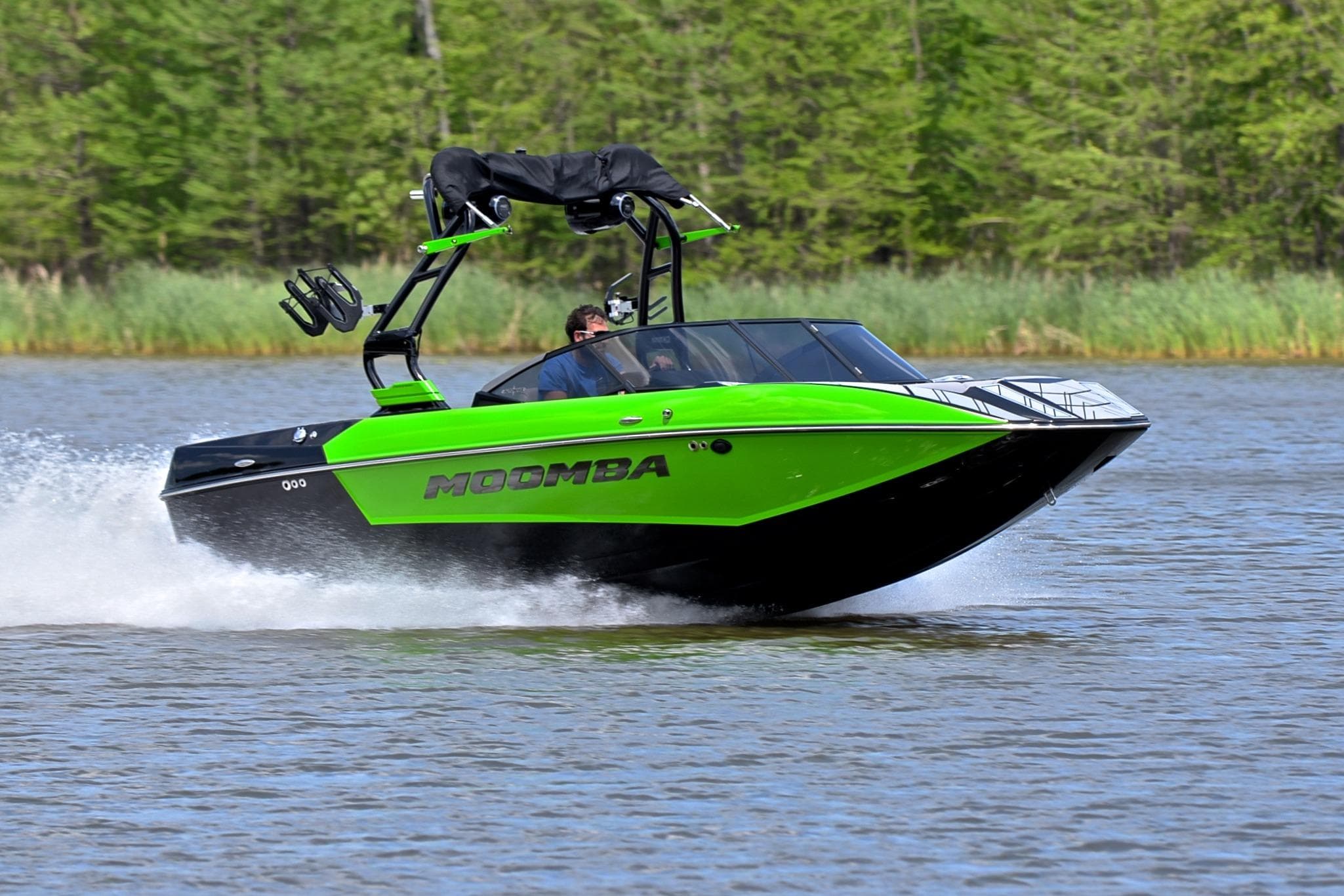 2024 Moomba Mondo boat speeding on a lake with lush green surroundings.