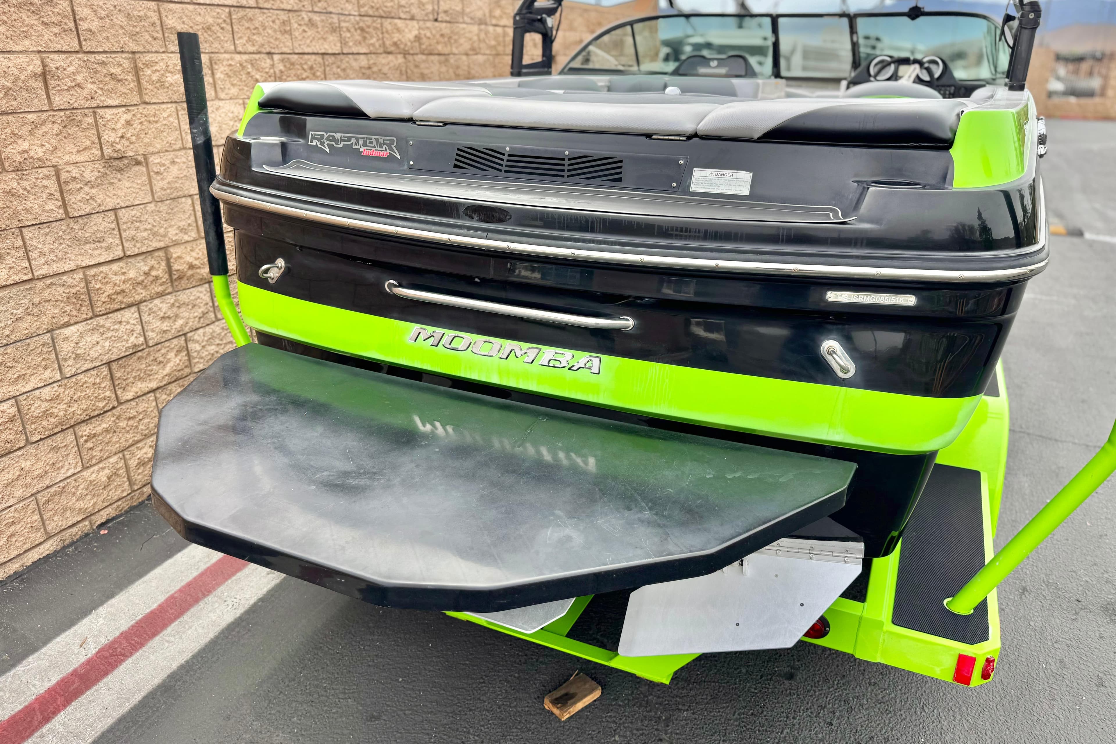 2016 Moomba Craz boat with vibrant green and black design, parked near a brick wall.