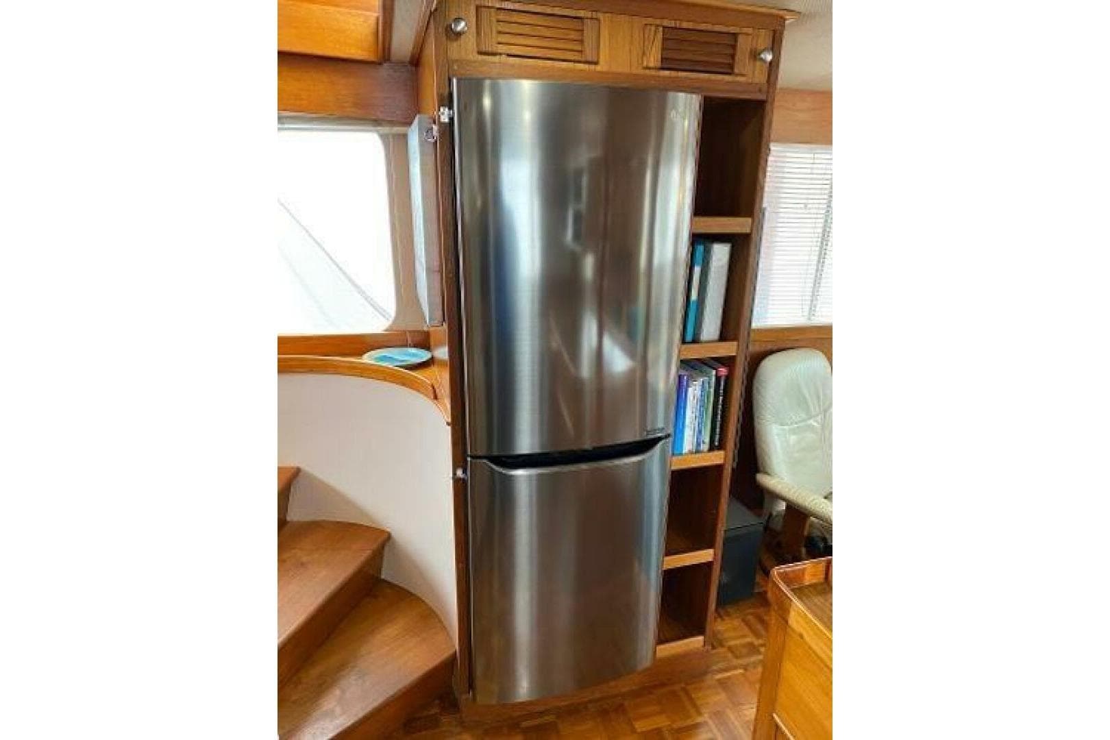 Stainless steel refrigerator in 1973 Grand Banks 49 Alaskan yacht interior, with wooden shelving.