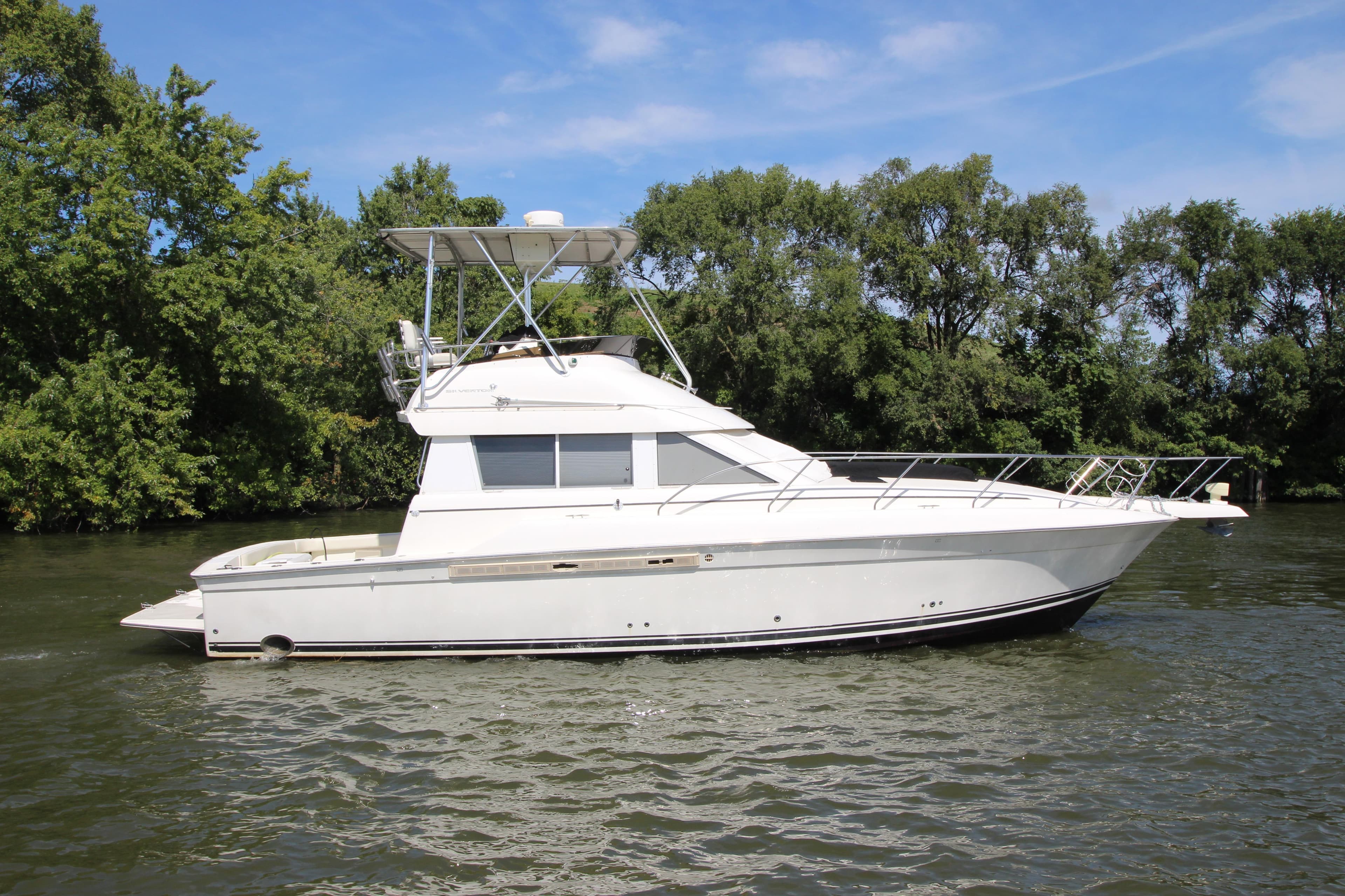 2000 Silverton 37 Convertible yacht cruising on a river with lush green trees.