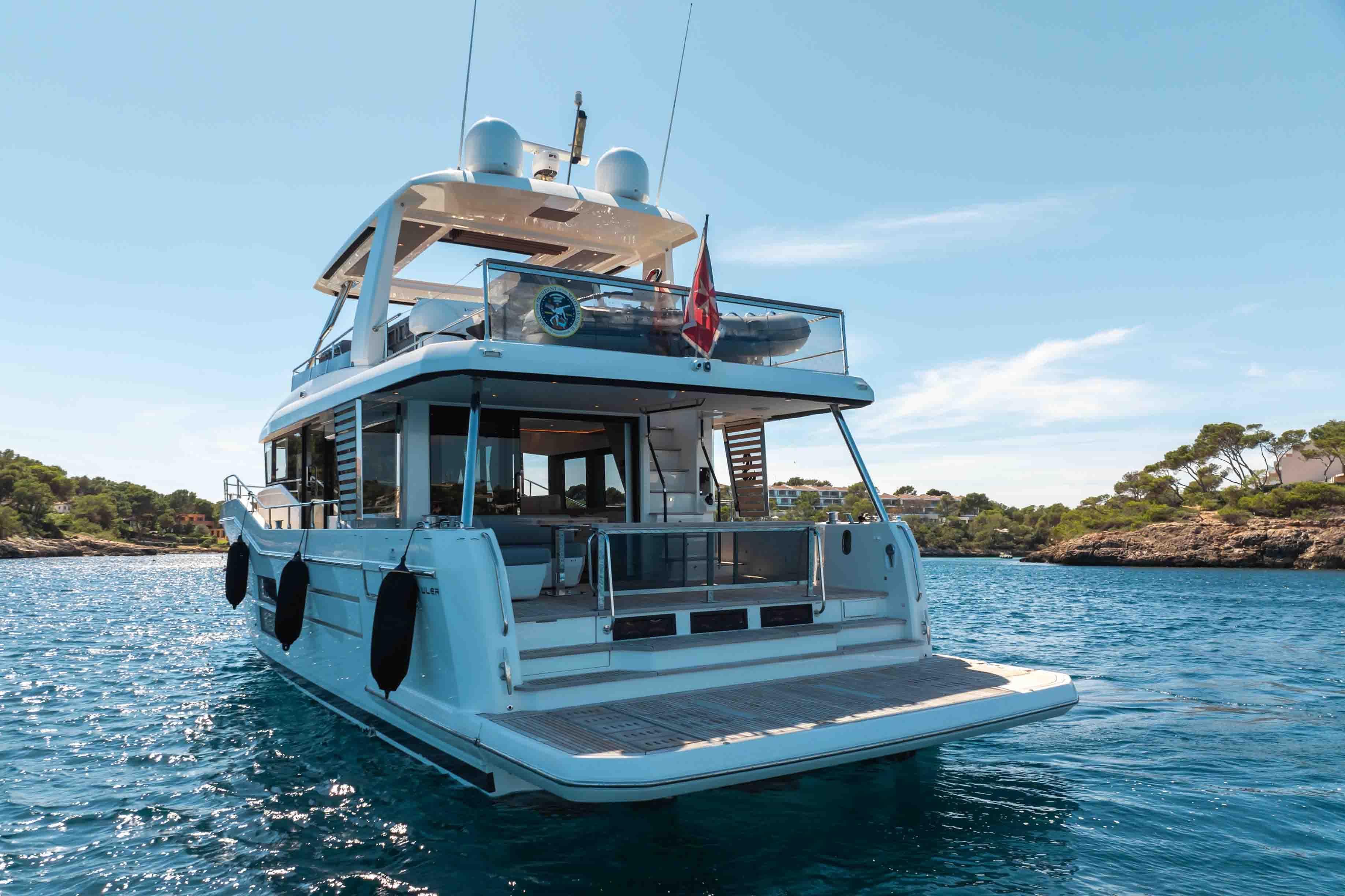 2023 Beneteau Grand Trawler 62 yacht on serene blue water, rear view.