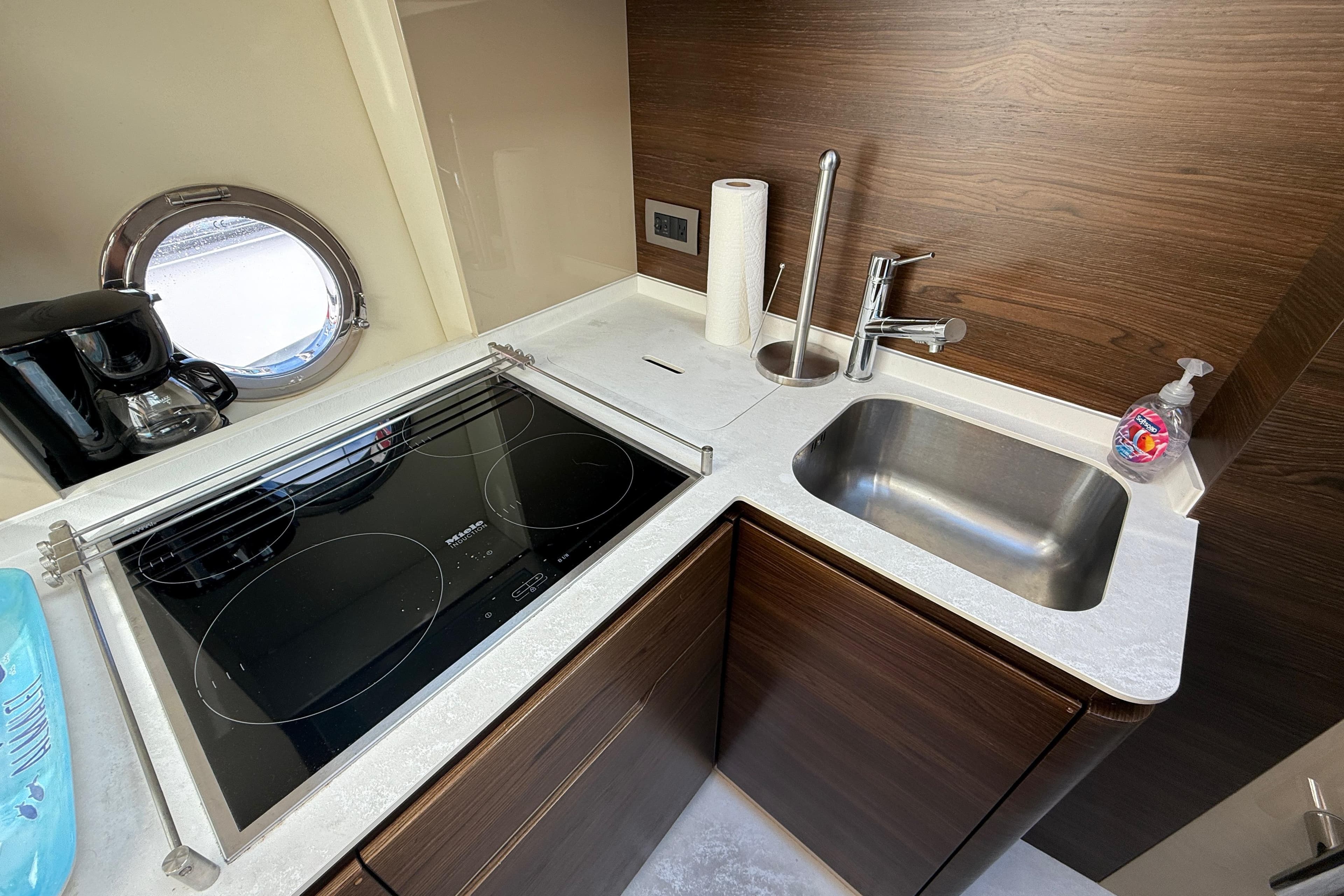 Modern kitchen in 2015 Azimut 50 yacht with stove, sink, and porthole window.