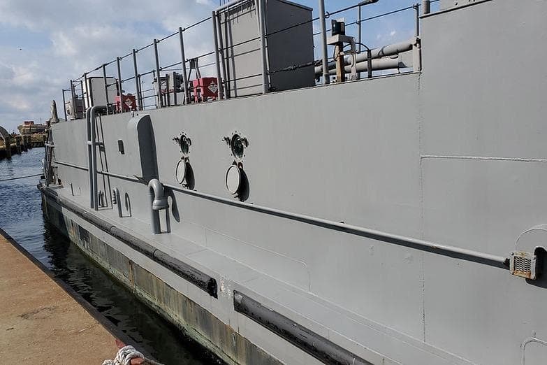 1970 COMMERICAL BOAT LCU-135 docked at a harbor, side view.