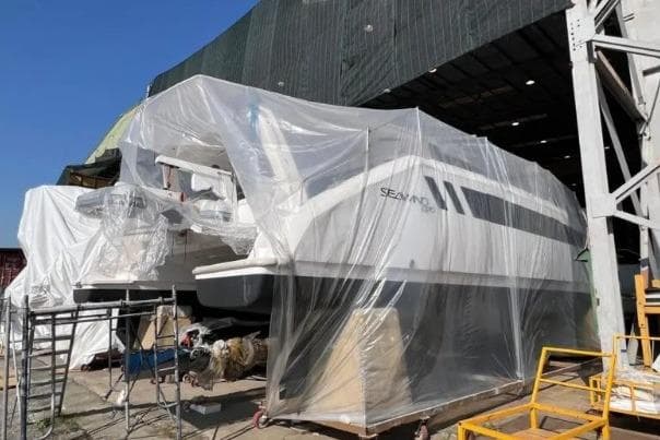 2026 Seawind 1370 catamaran under construction, covered in protective plastic in a shipyard.