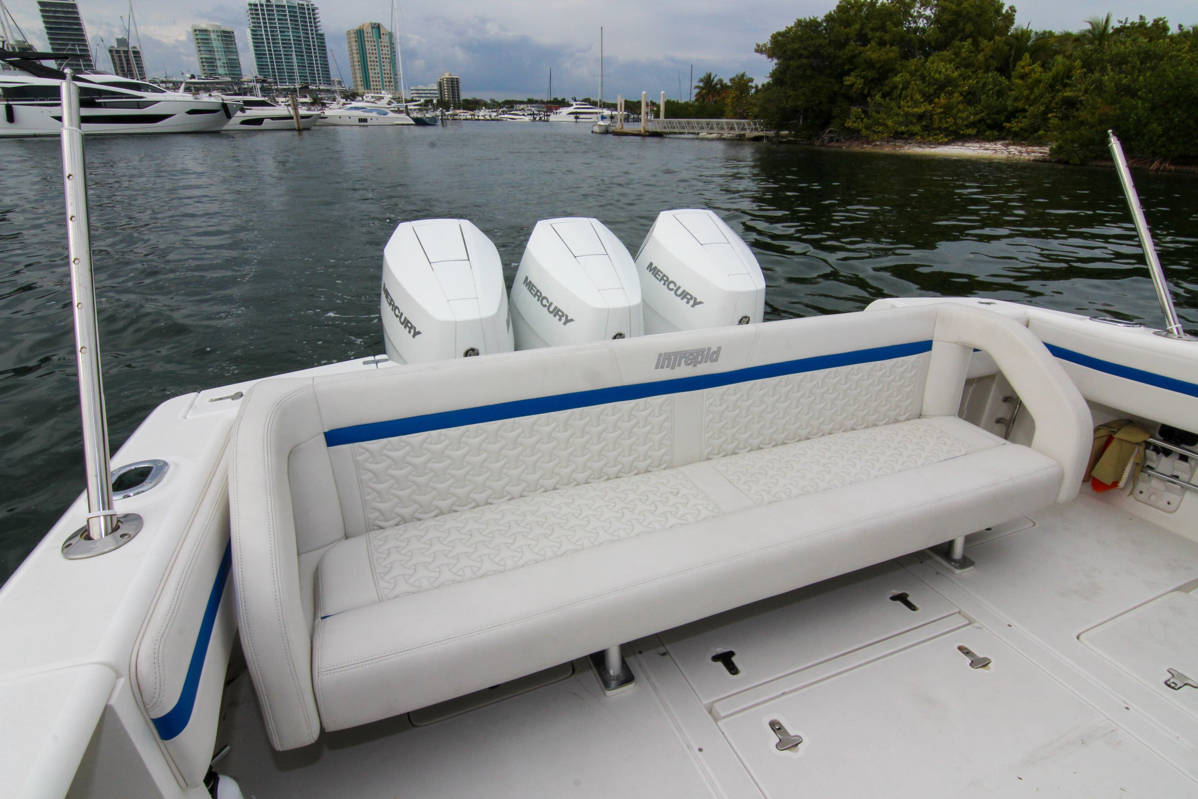 2003 Intrepid 377 Walkaround boat with triple Mercury engines, docked near luxury yachts.
