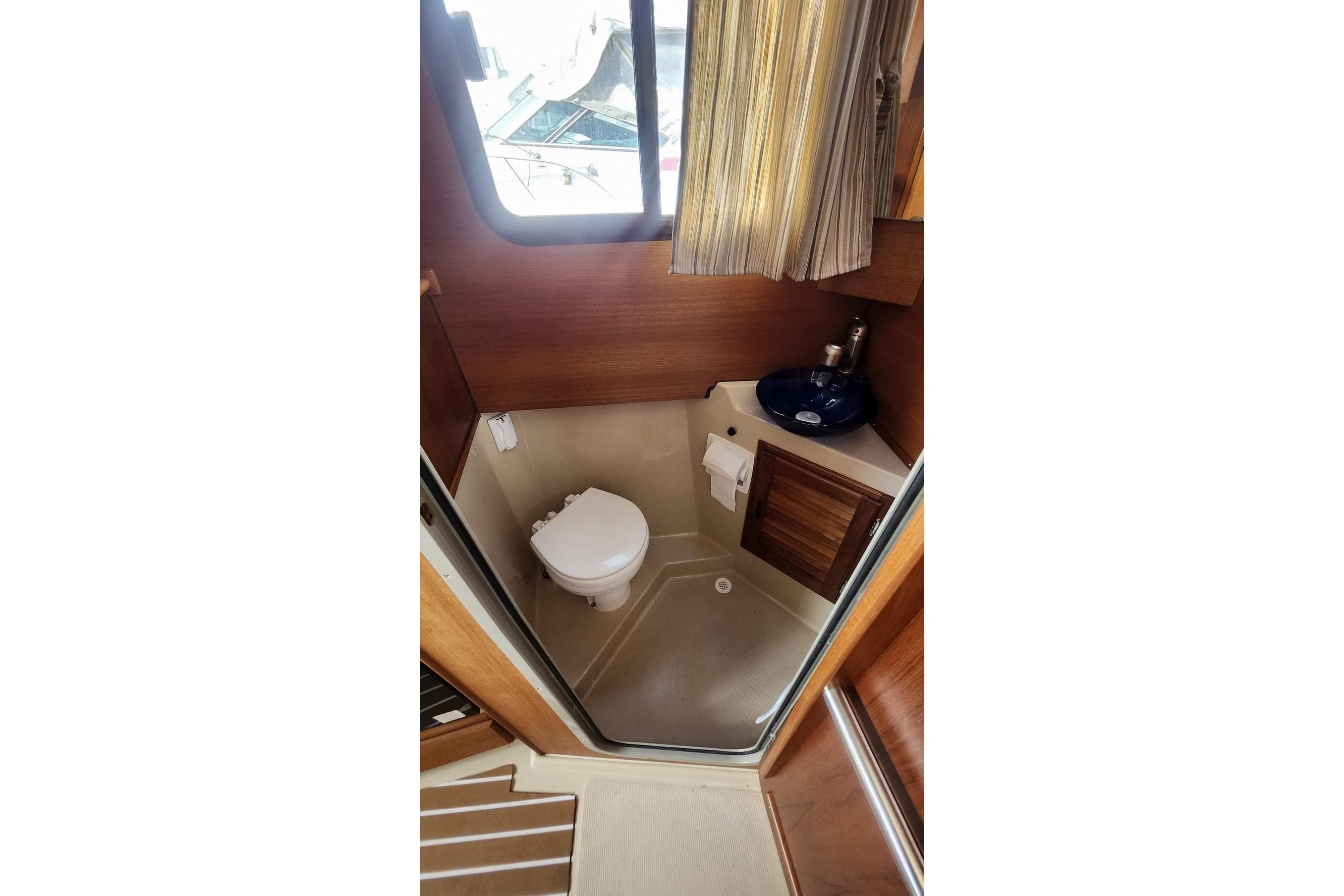 2014 Ranger Tugs R-27 boat bathroom with toilet, sink, and wooden cabinetry.