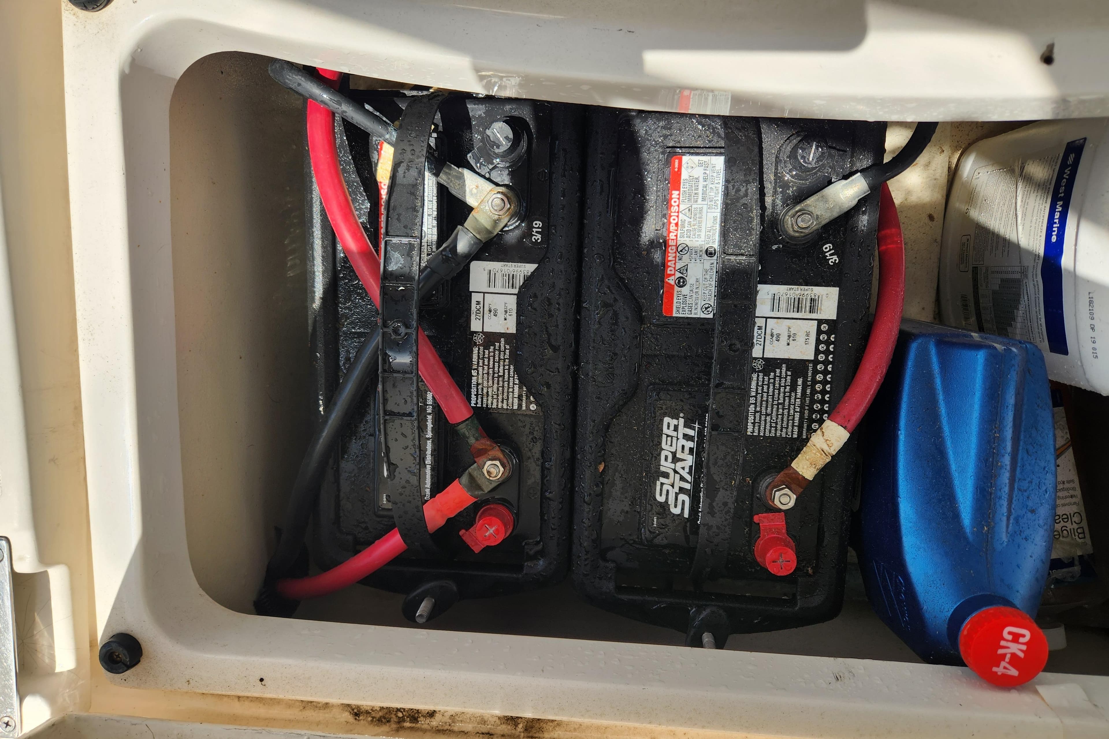 Battery compartment of a 1997 Hunter 340 sailboat with connected cables and oil container.