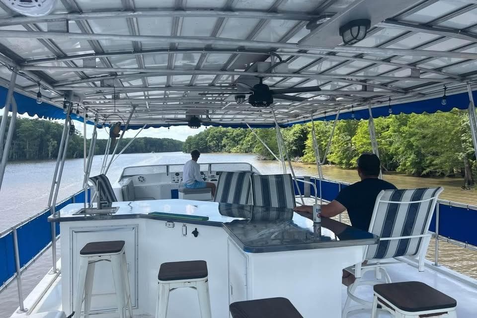 1999 Sharpe houseboat cruising on a river, featuring a spacious deck with seating and canopy.