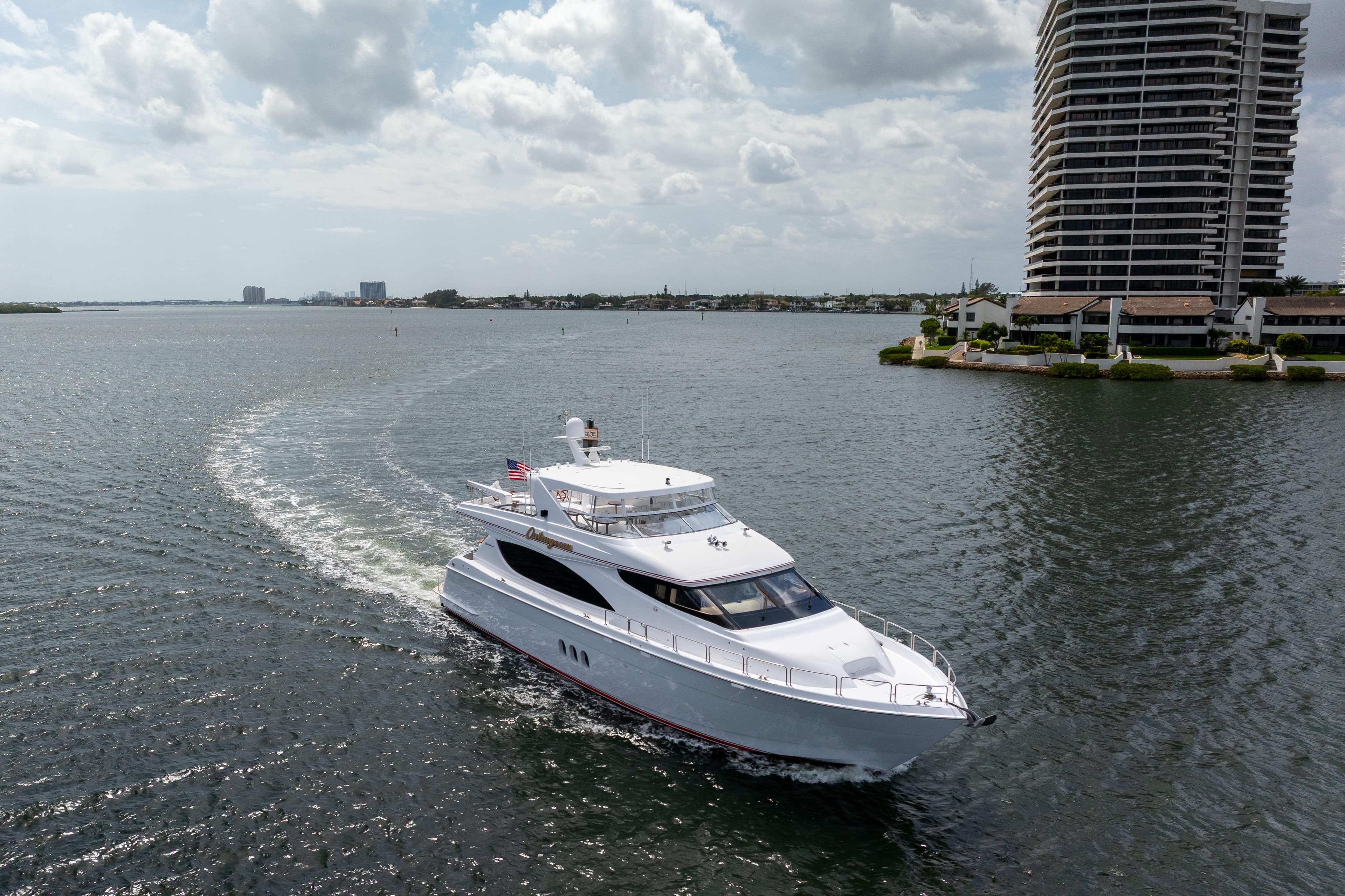 2005 Hatteras 80 Motor Yacht cruising near waterfront buildings under cloudy sky.