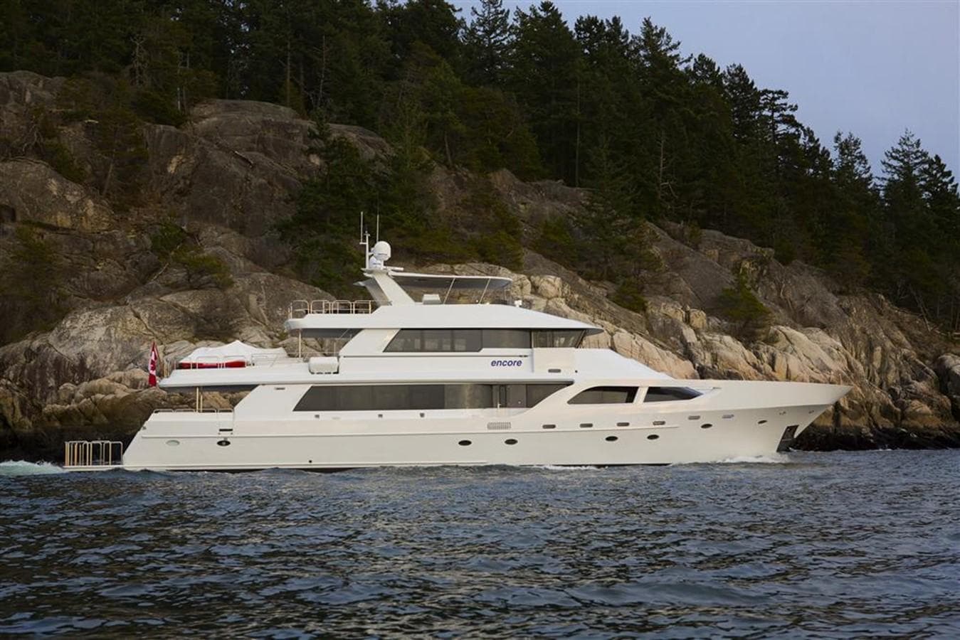 Luxurious 1992 Crescent Custom yacht cruising near rocky shoreline and forested landscape.