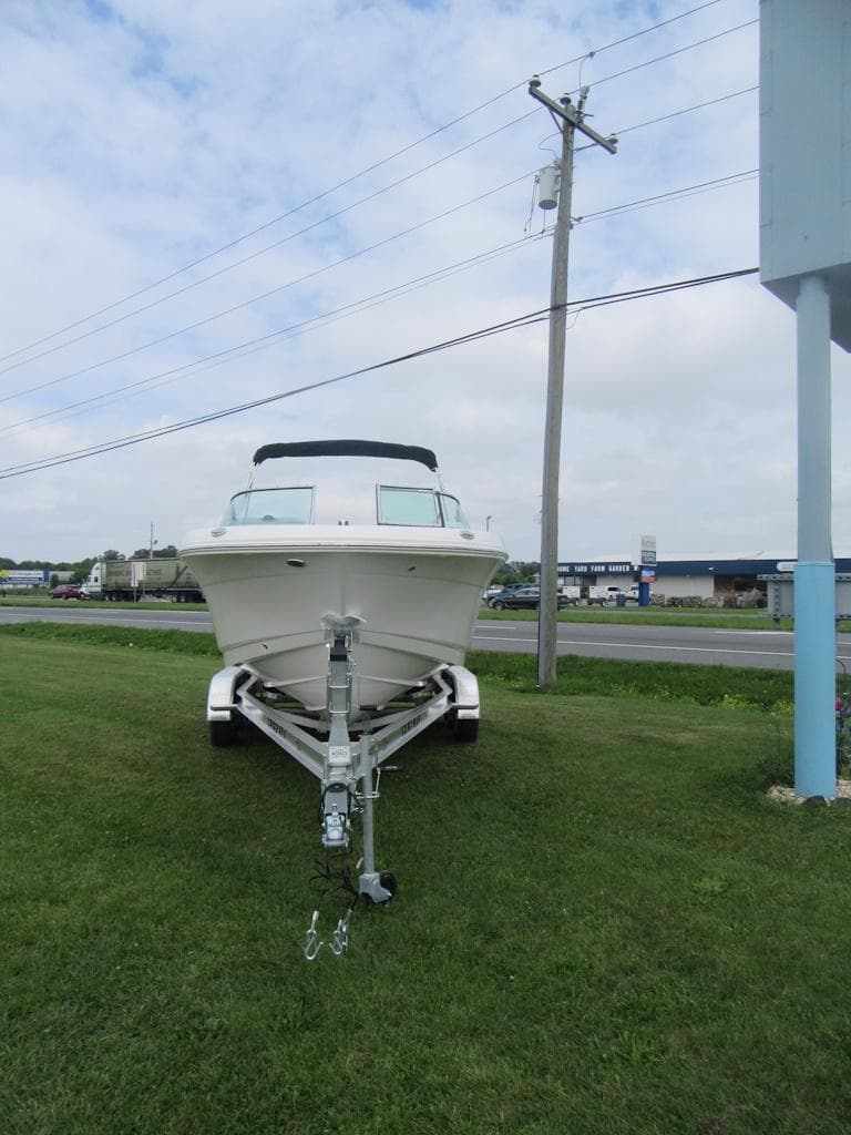 2025 Robalo R207 Dual Console boat on trailer, parked on grass near road.