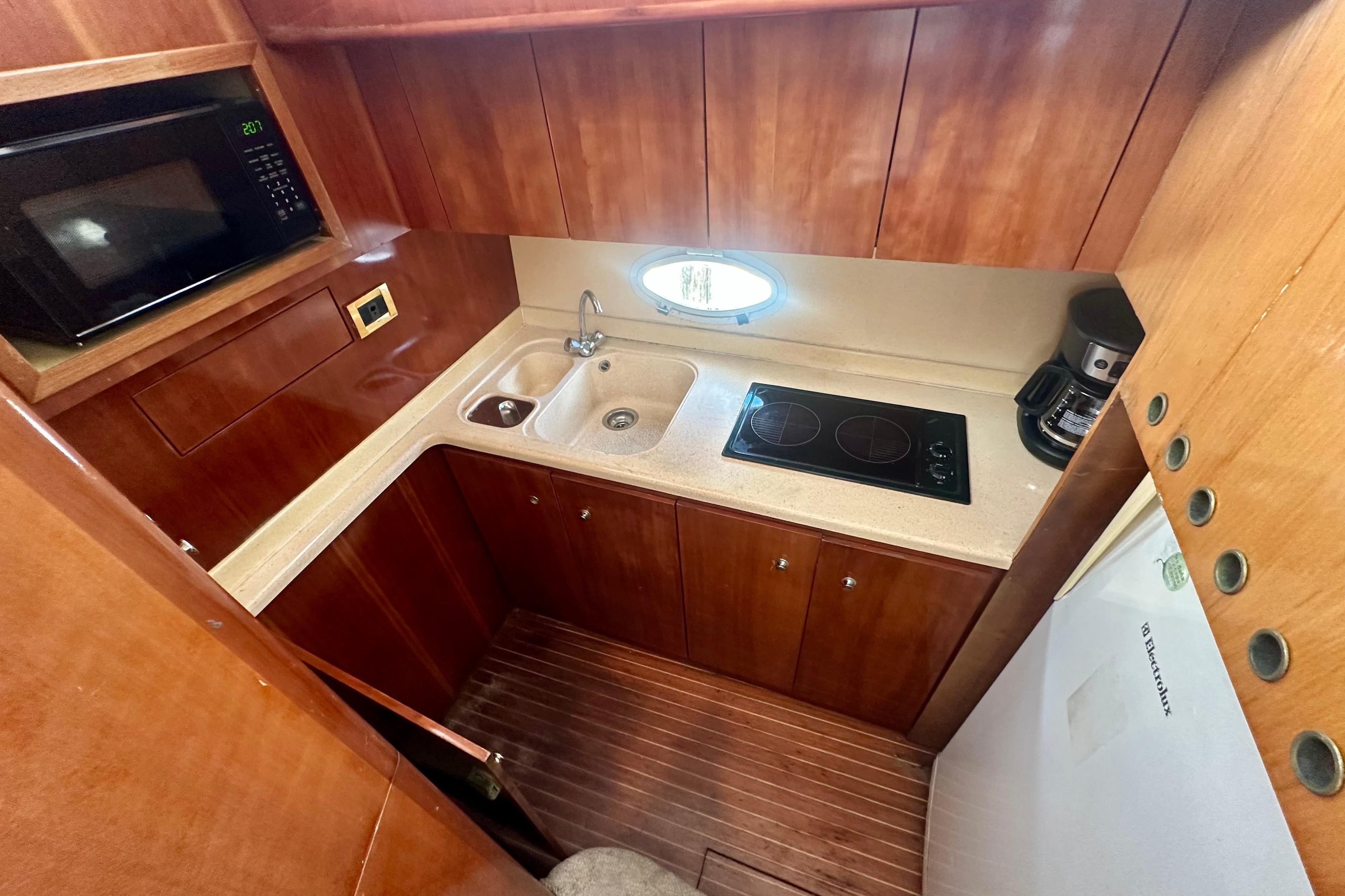 Compact kitchen in a 1999 Azimut 58 yacht with stove, sink, and microwave.