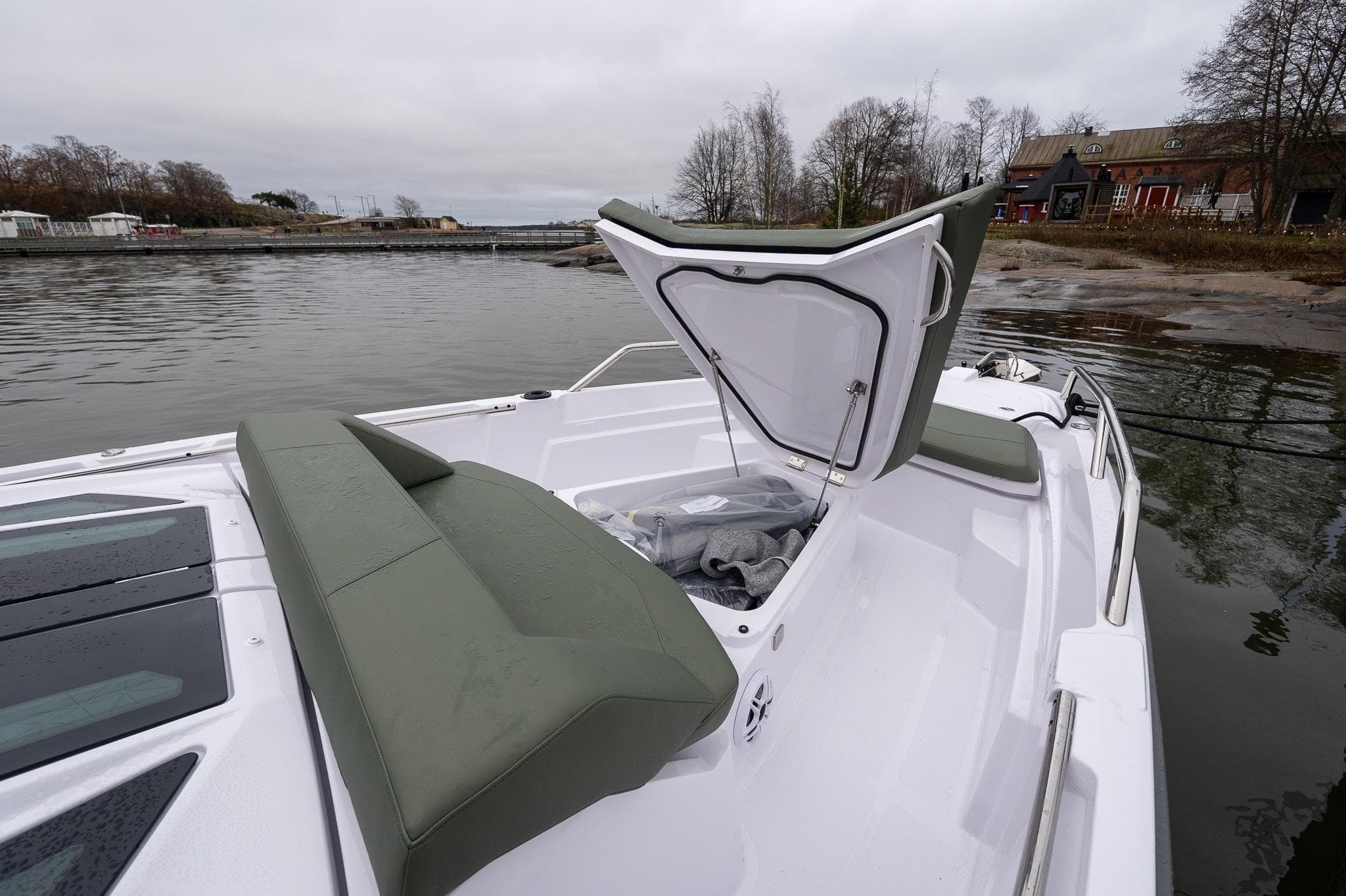 2027 Axopar 38 Cross Cabin boat with open storage compartment, docked by a scenic shoreline.