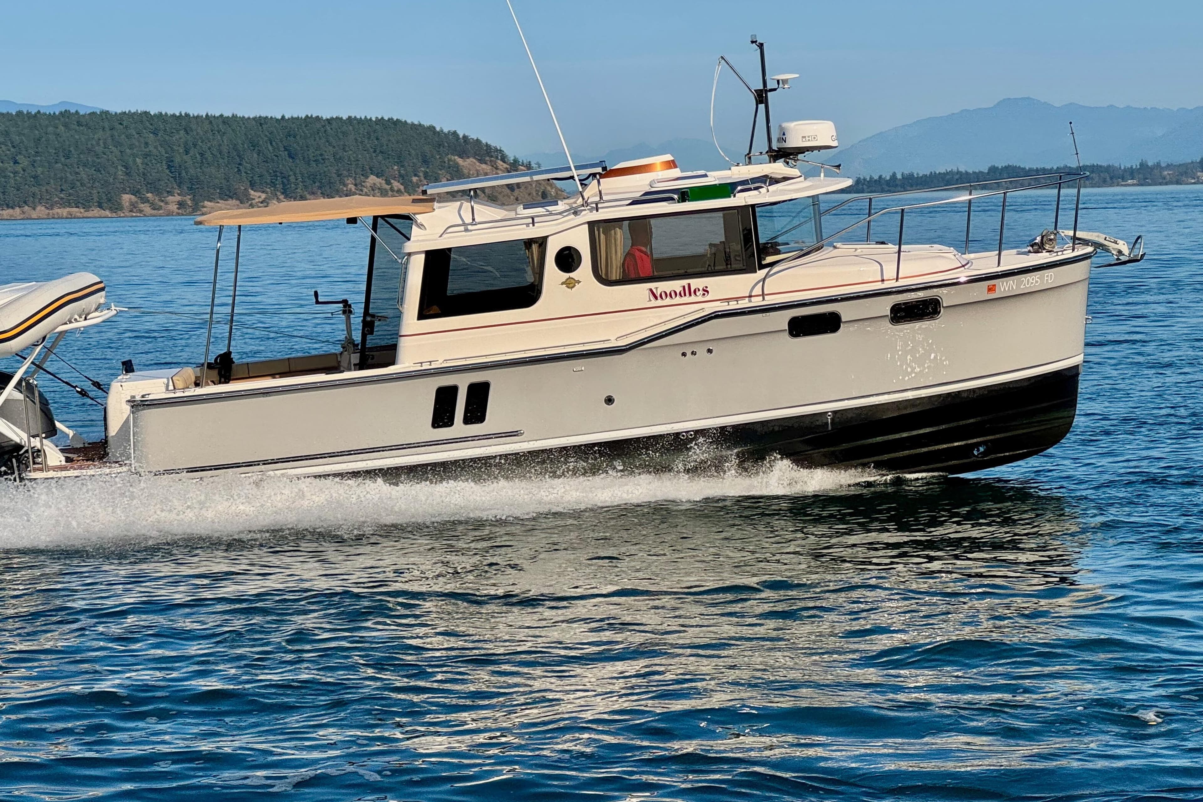 2024 Ranger Tugs R-27 cruising on a scenic lake with forested hills in the background.