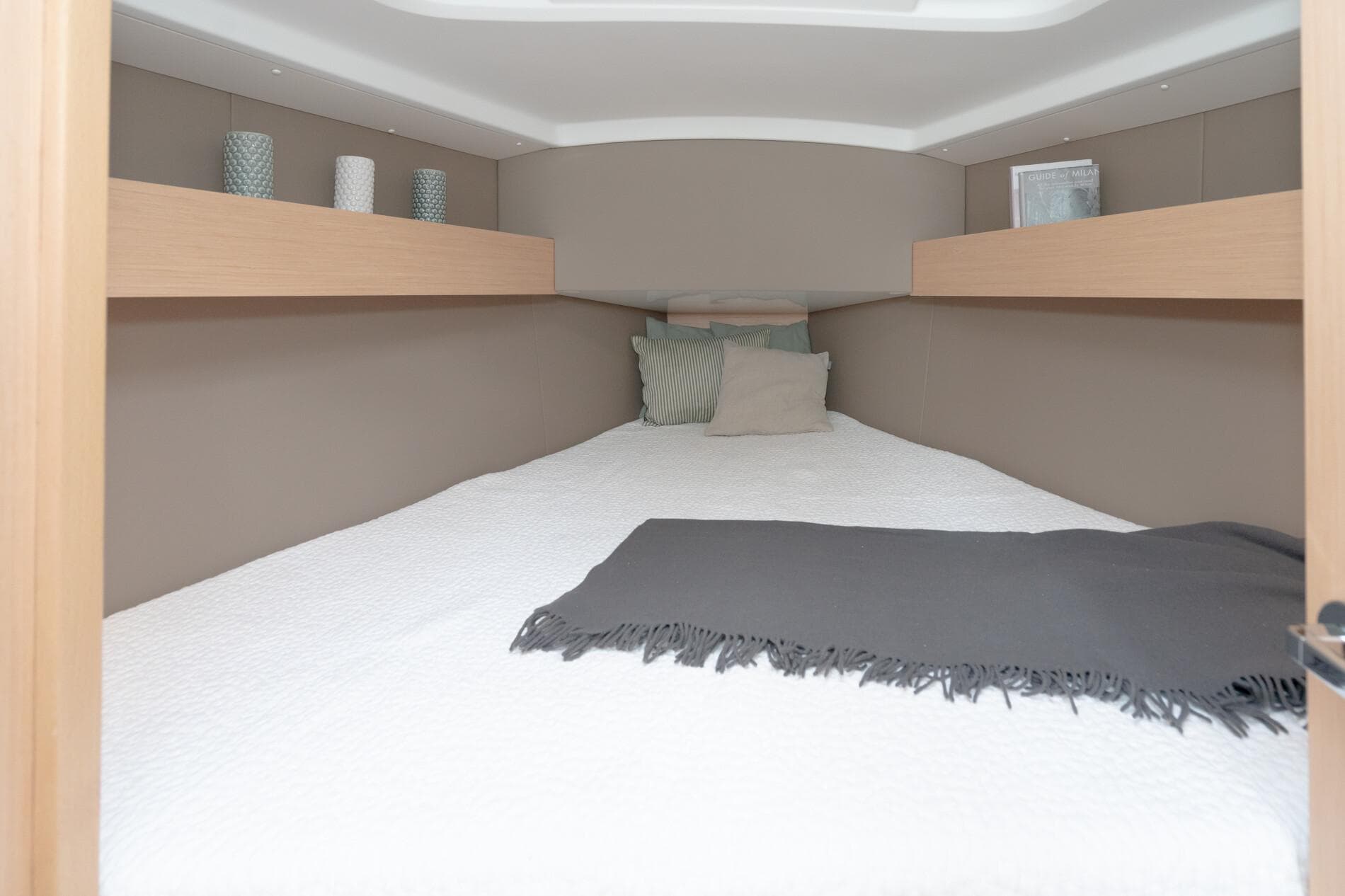 Cozy cabin interior of 2024 Beneteau Oceanis 30.1 with bed and decorative shelves.