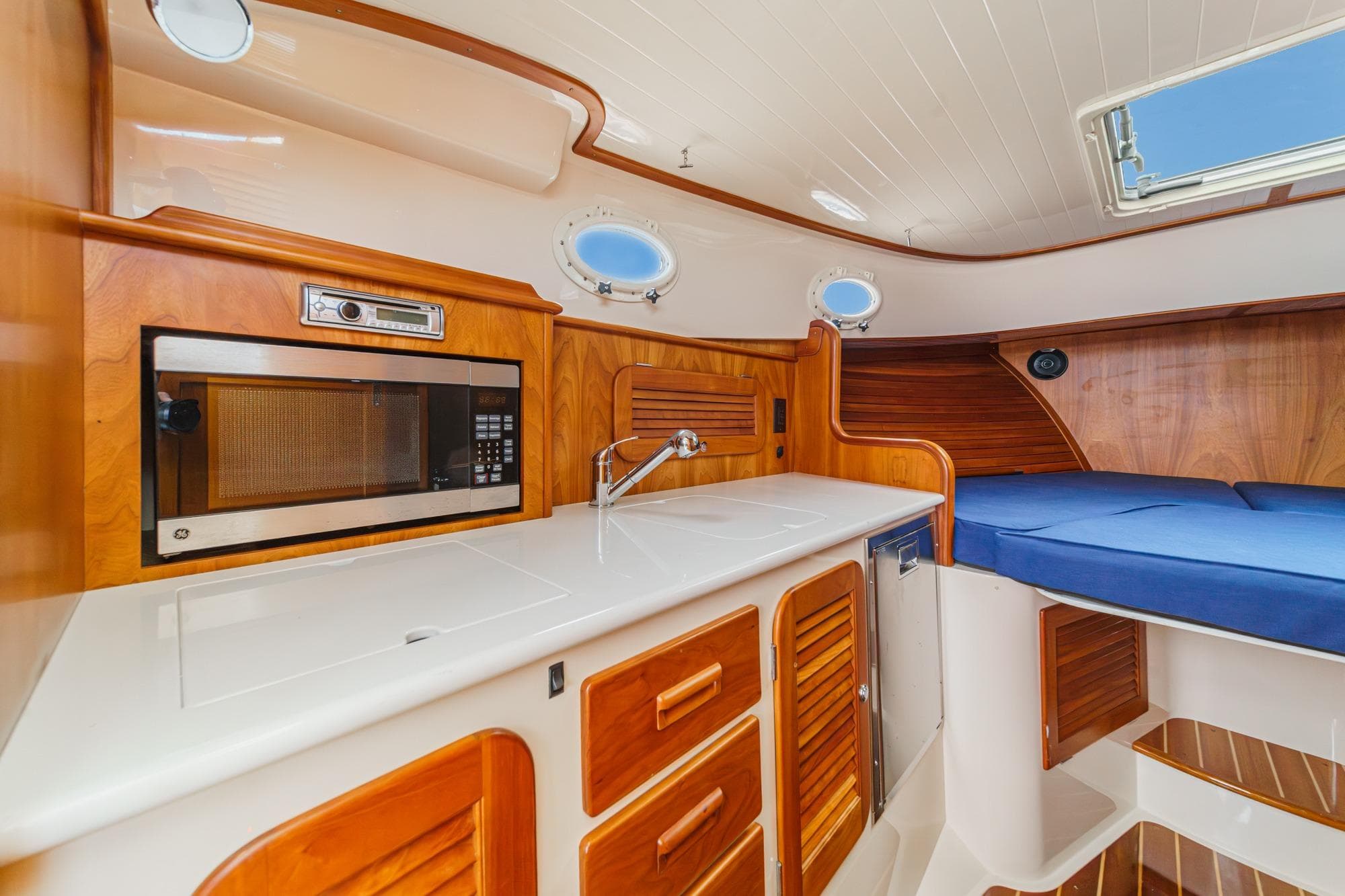 2014 Hinckley Talaria 34 interior with wood cabinetry, microwave, sink, and blue cushioned seating.