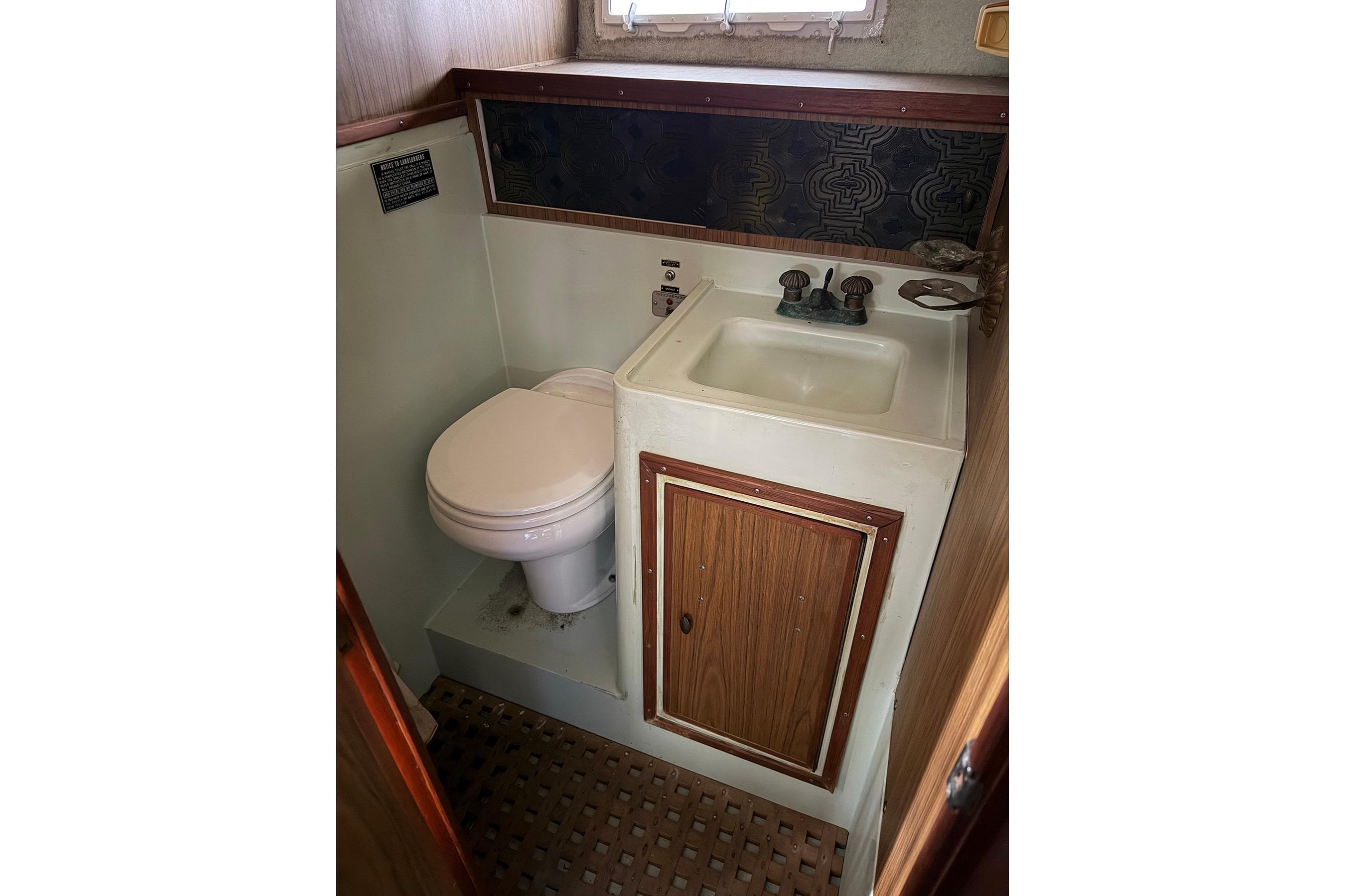 1974 Magnum Sportfisher boat bathroom with toilet, sink, and wooden cabinetry.