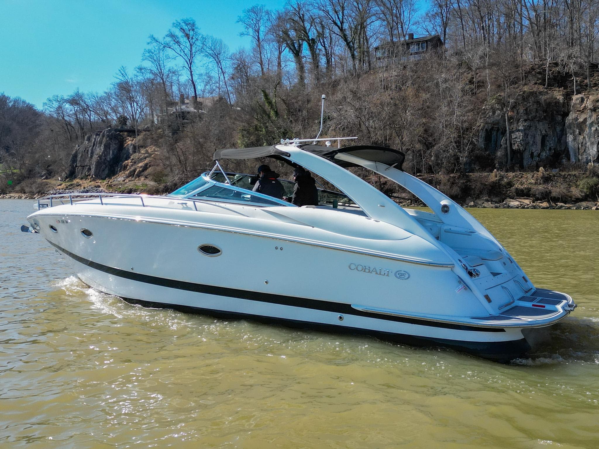 2004 Cobalt 360 boat cruising on a river with wooded shoreline.