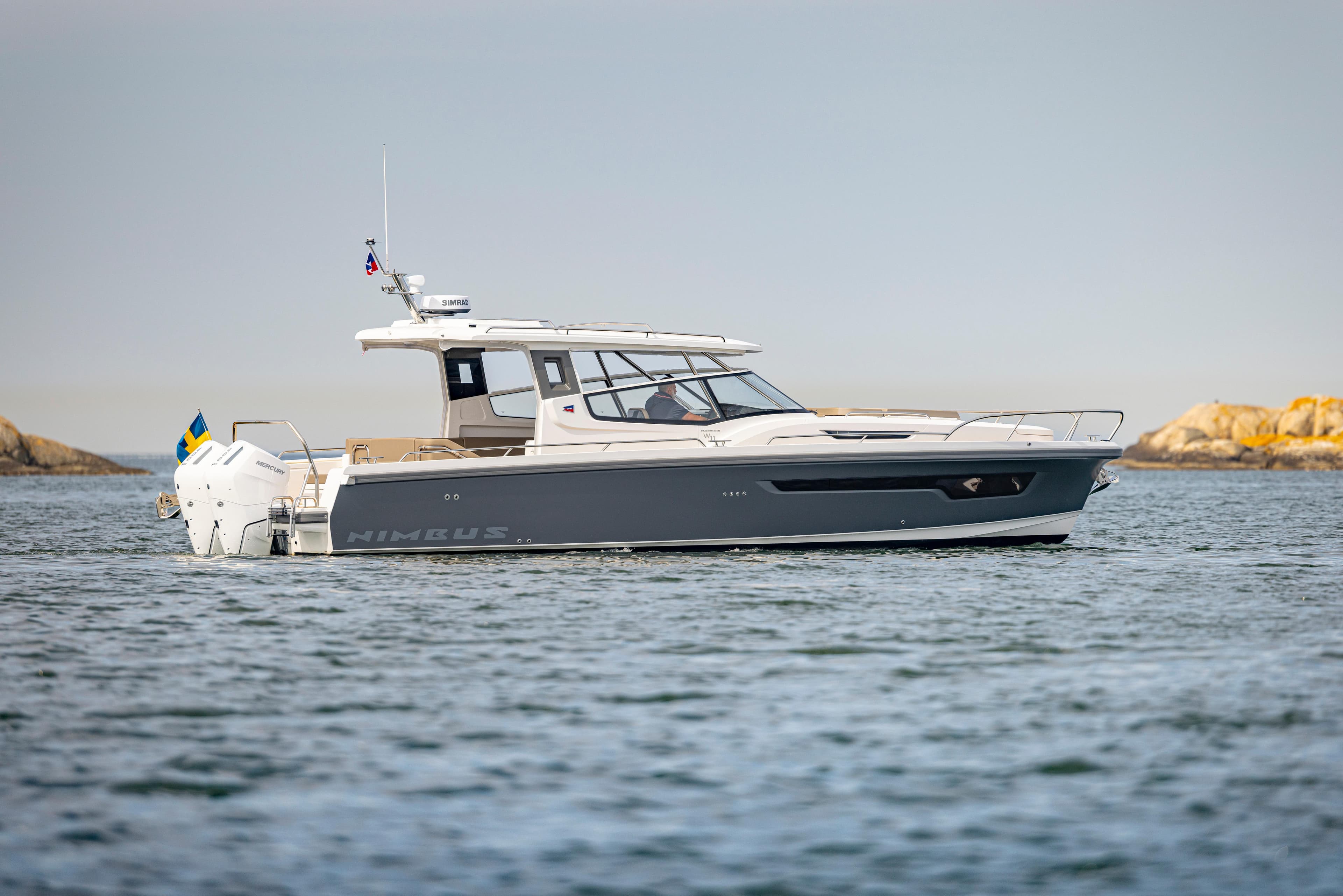 2025 Nimbus W11 boat cruising on calm waters near rocky shoreline.