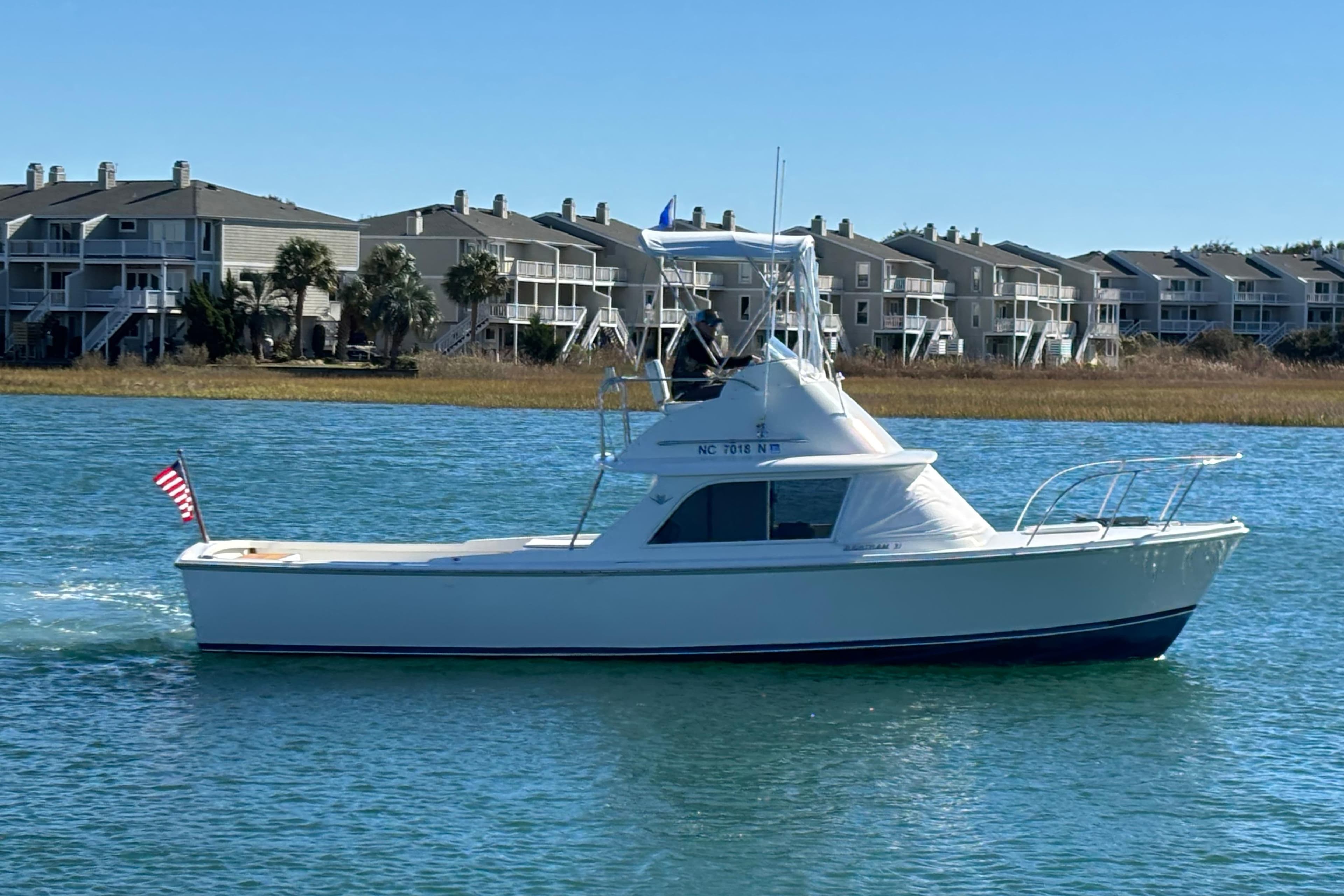 1970 Bertram 31 Flybridge Cruiser on water, with residential buildings in background.