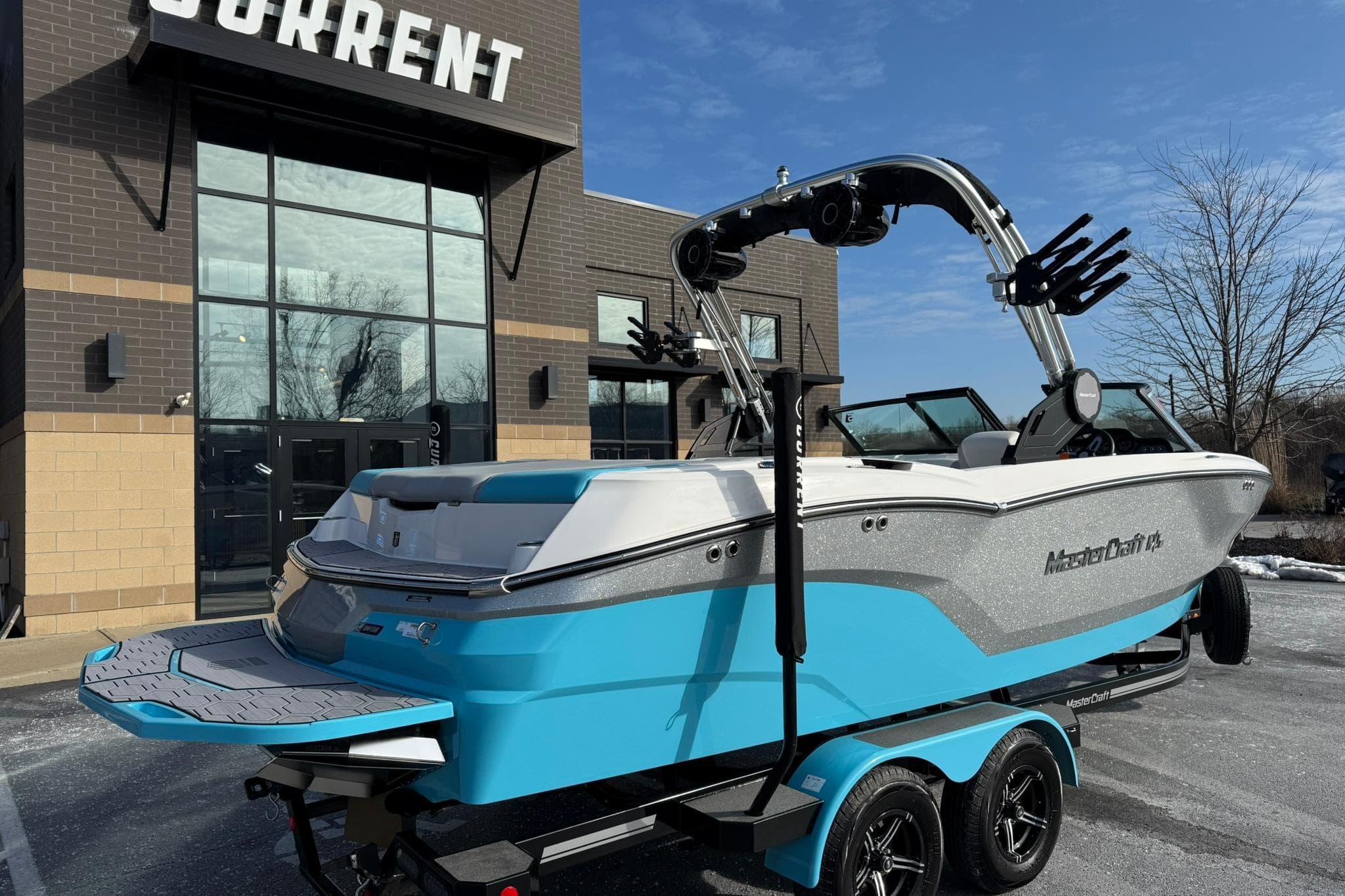 2023 MasterCraft NXT23 boat in blue and white, parked outside a modern building.