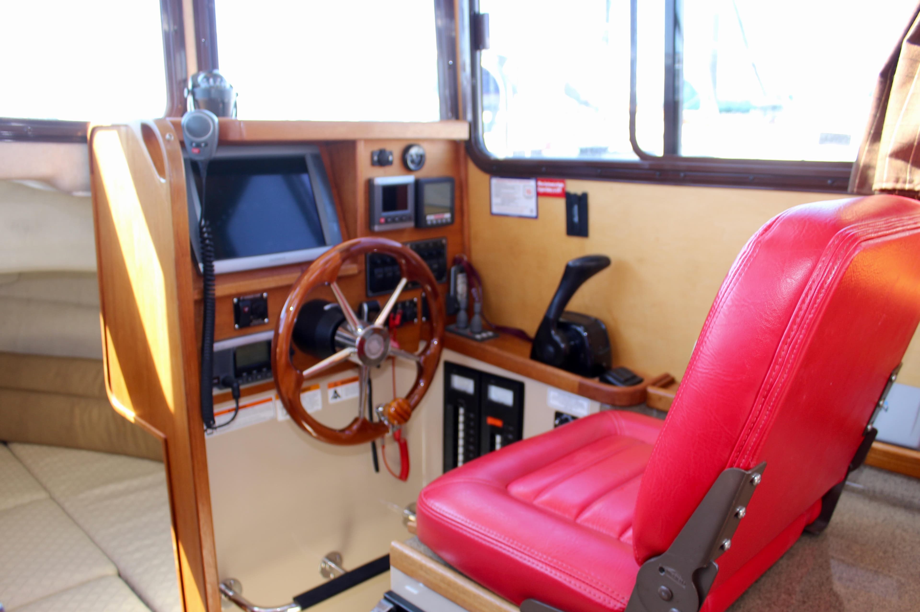 Interior of 2011 Ranger Tugs R-27 boat with red captain's chair and wooden steering wheel.