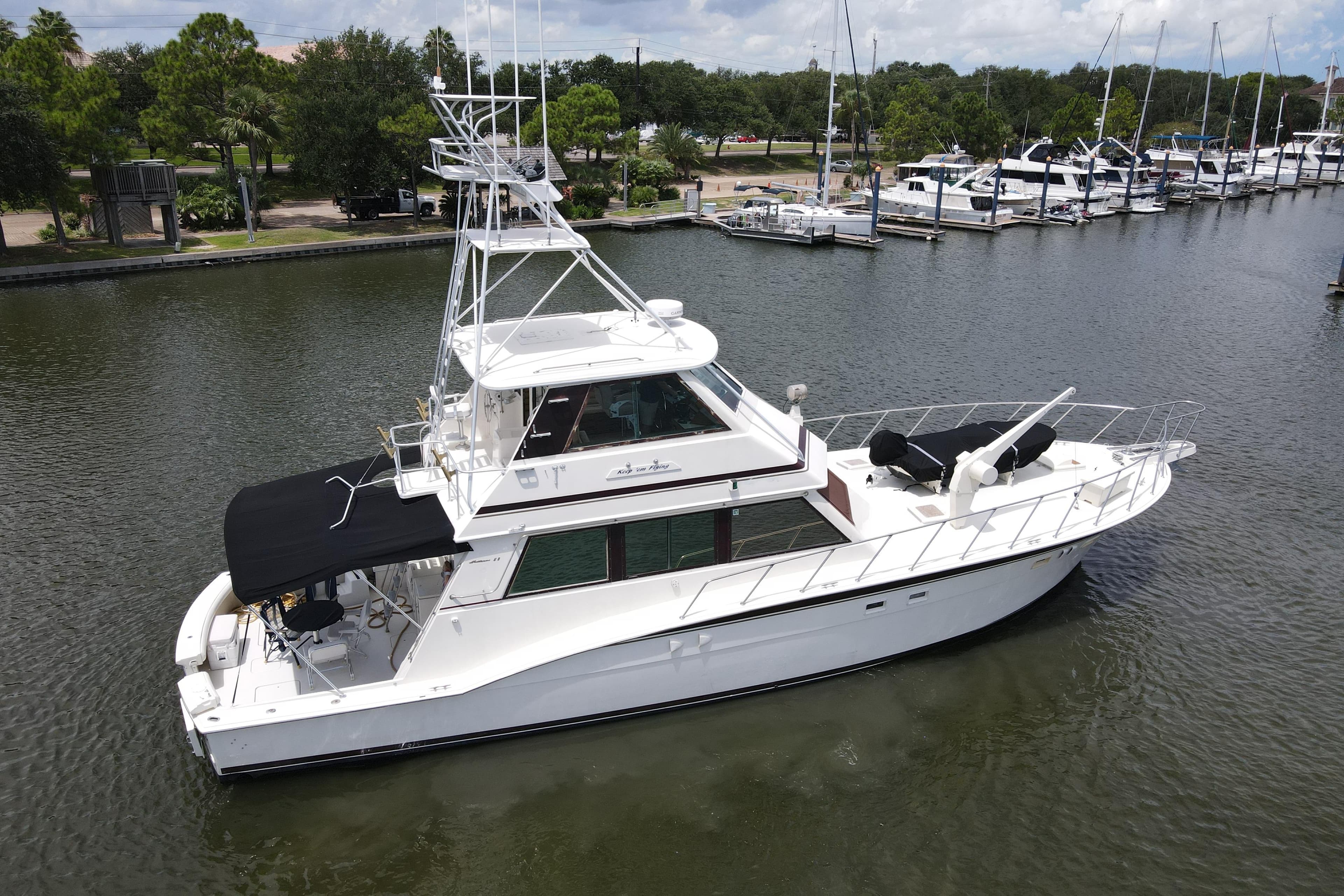 1985 Hatteras 60 Convertible yacht docked in a marina, surrounded by water and other boats.