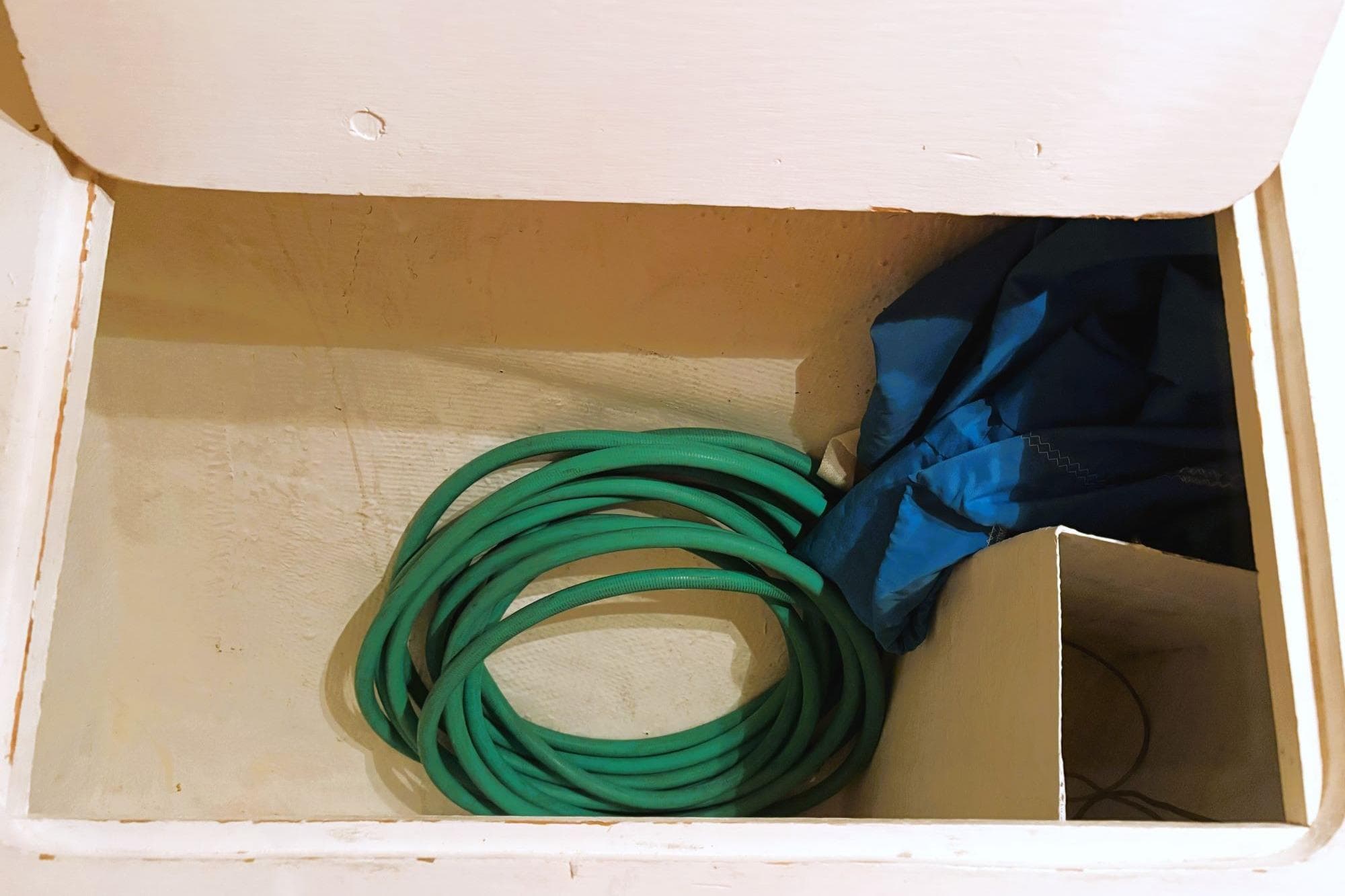 Storage compartment with green hose and blue fabric inside a Discovery 42, 1980 model.