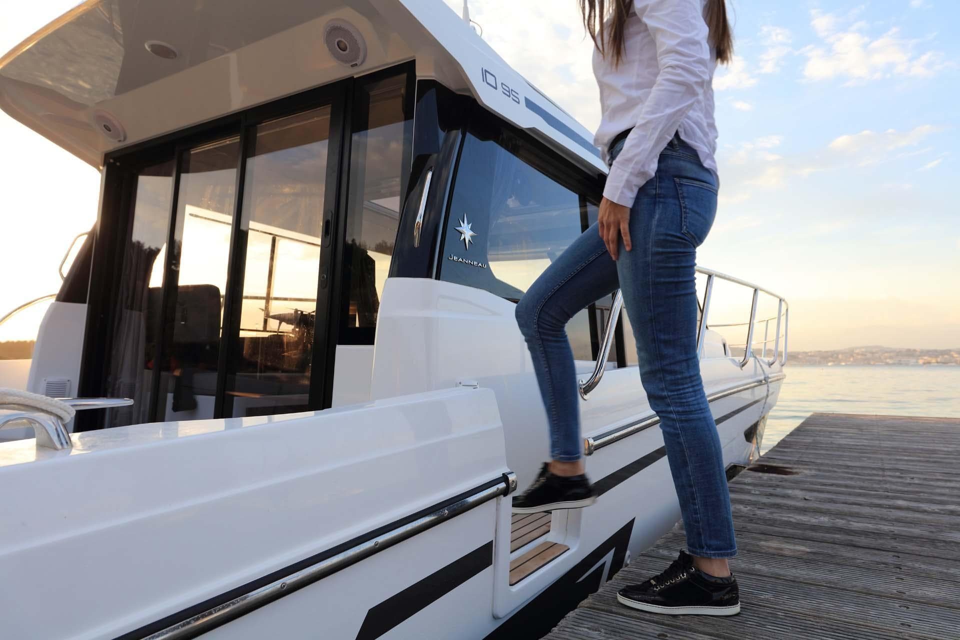 Woman boarding 2024 Jeanneau NC 1095 boat at sunset on a dock.