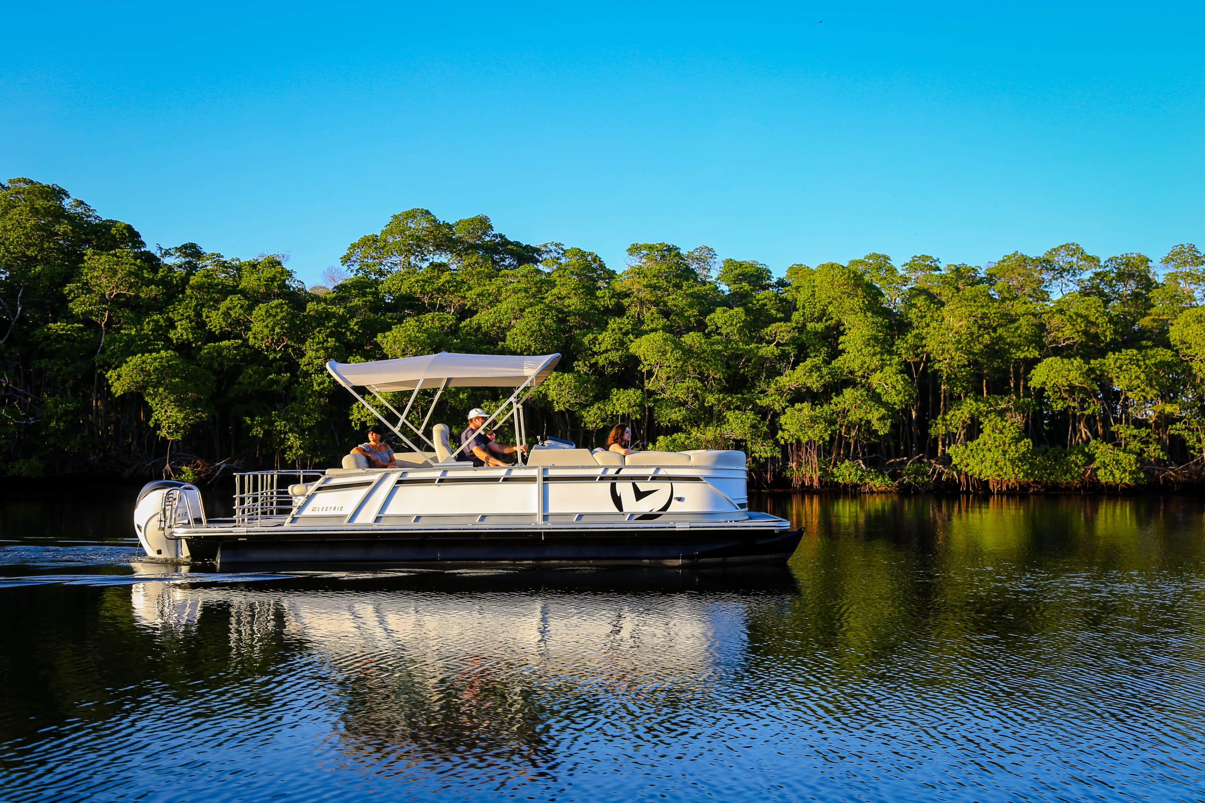 2025 Vision Marine Technologies V24 boat cruising on a serene lake with lush green trees.