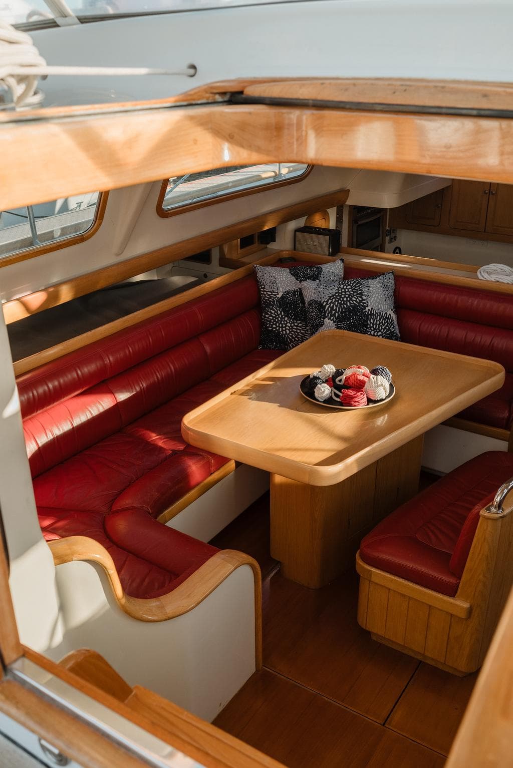 Interior of 1993 Dubois 78 yacht with red leather seating and wooden table.
