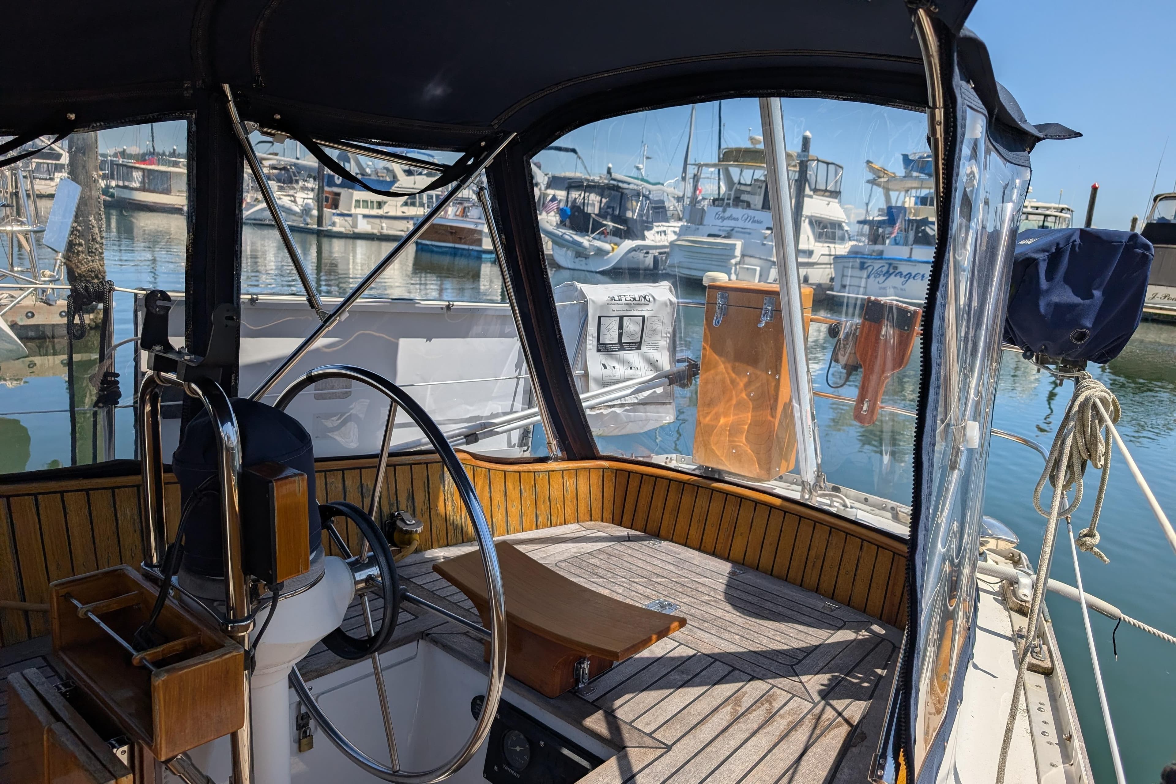 Cockpit of 1984 Ohlson 38 sailboat docked at marina, featuring steering wheel and clear canopy.