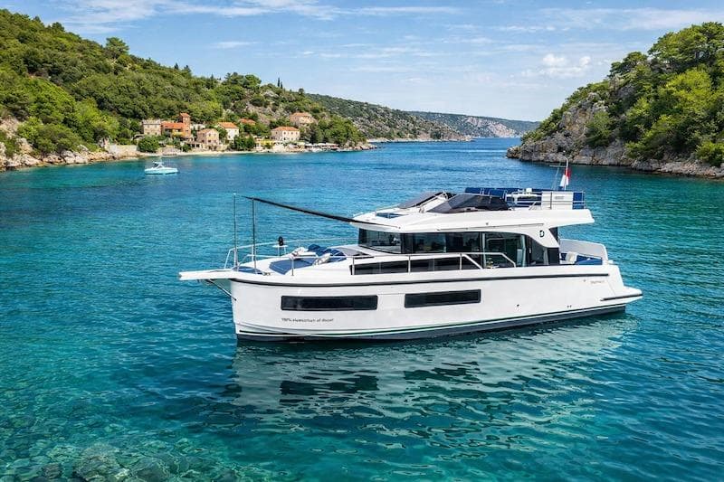 2026 Delphia 11 Flylounge yacht cruising in a scenic, clear blue water bay.